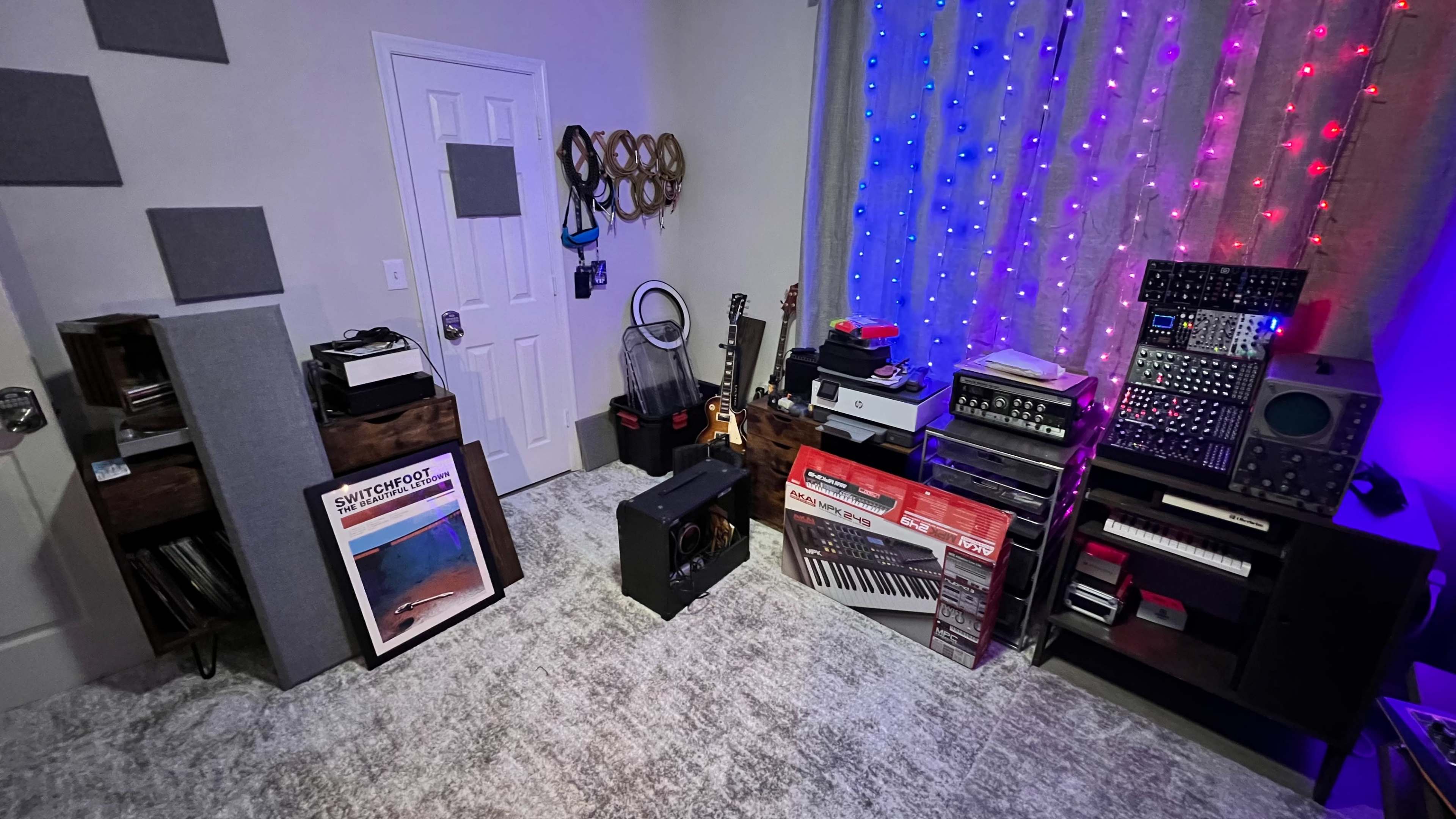 A room filled with various musical instruments and audio equipment, including guitars, synthesizers, and amplifiers, alongside decorative string lights.