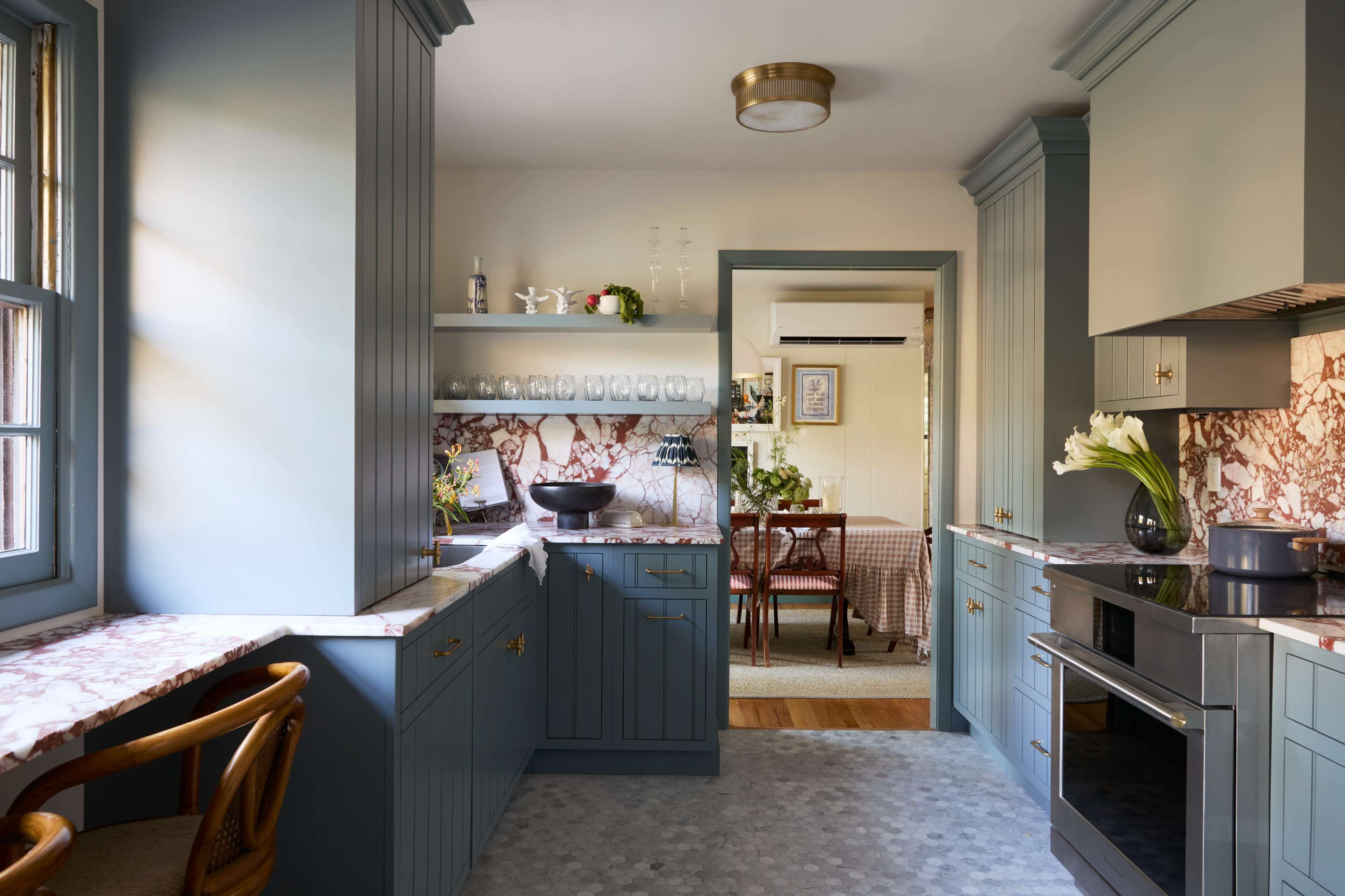 The image shows a modern kitchen with blue cabinetry, marble countertops, and a view into a dining area.