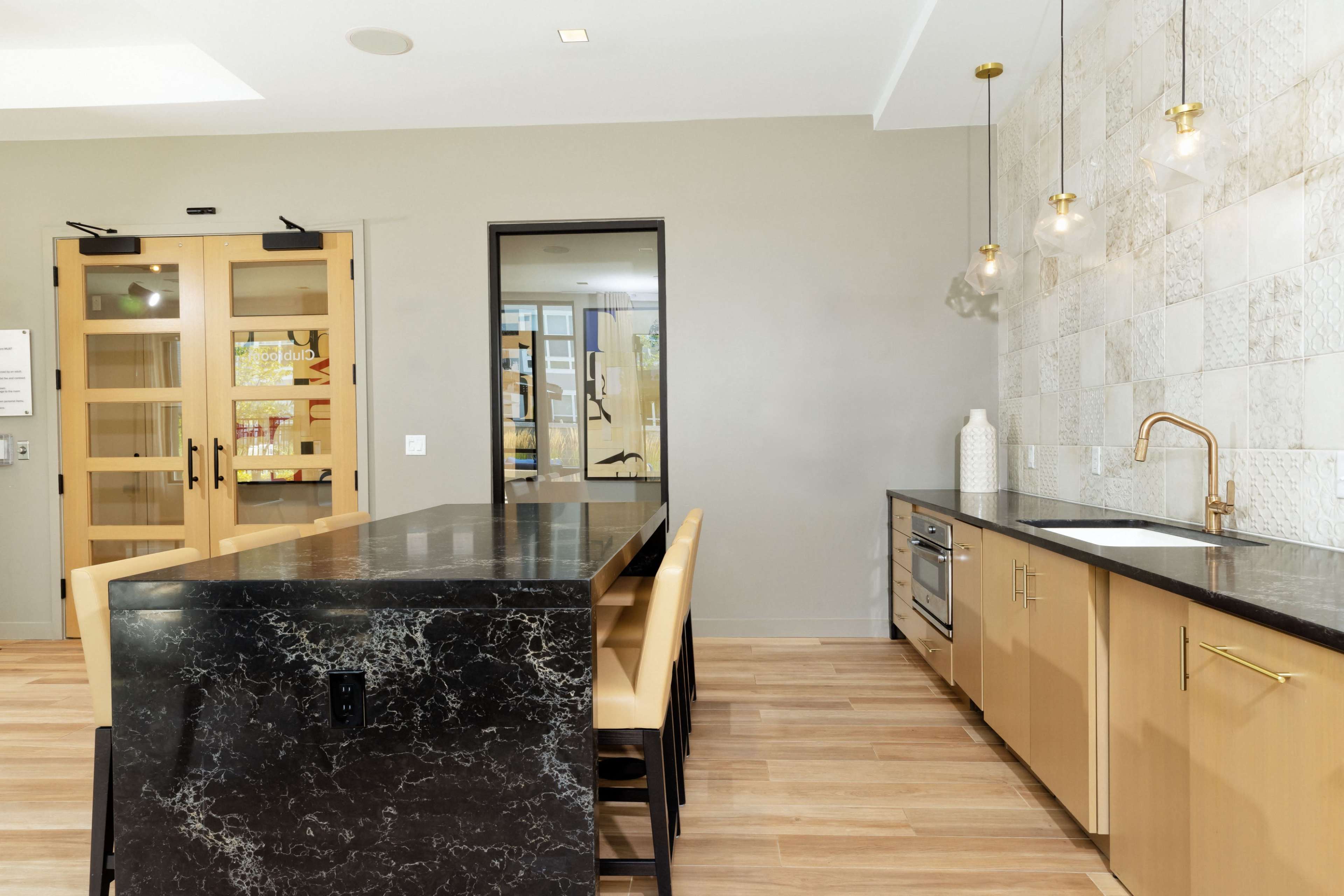 A modern kitchen with a large black marble island, wooden cabinetry, and pendant lighting against a textured wall.