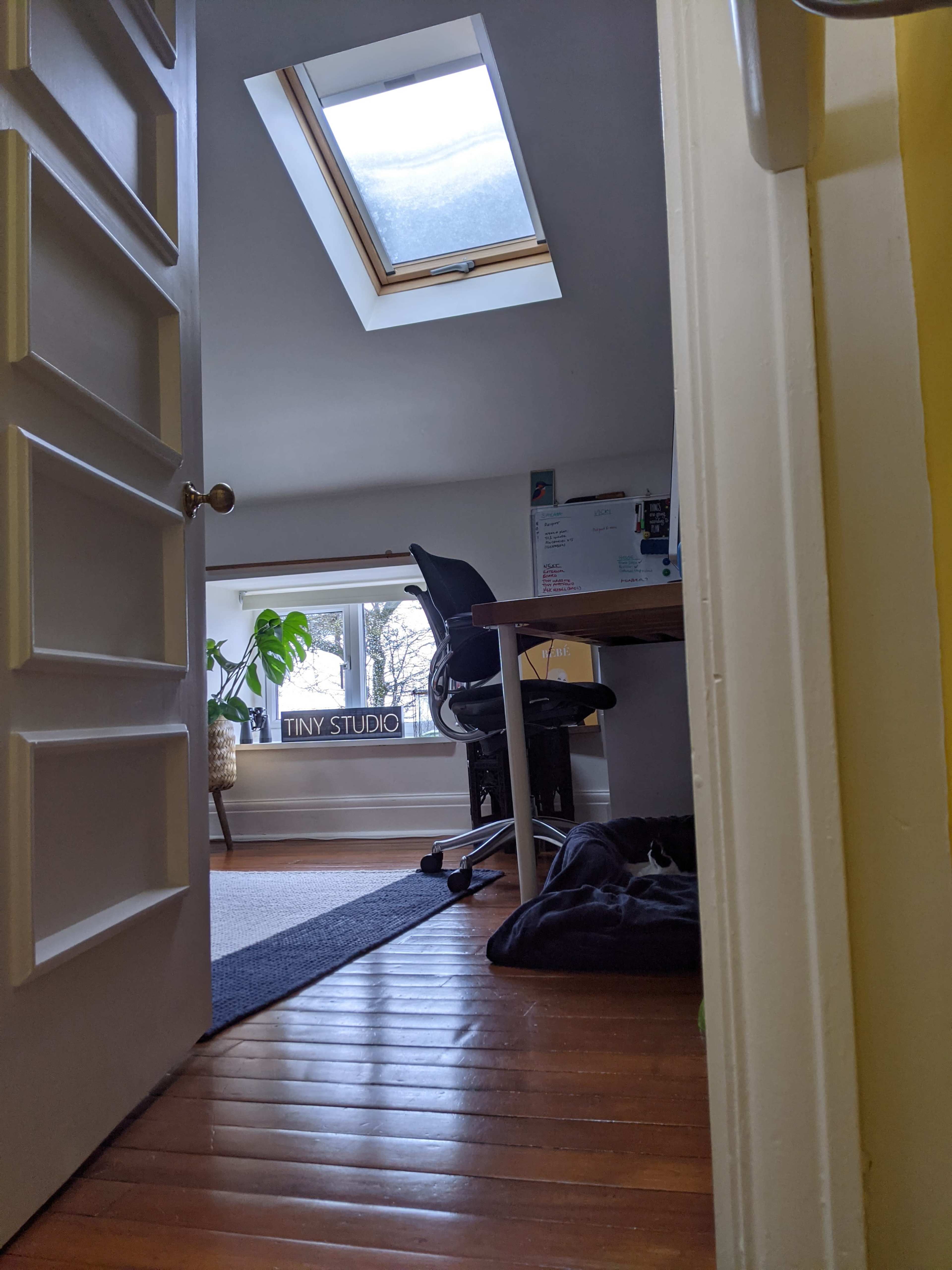 A partially open door reveals a small studio with a desk and chair under a skylight.