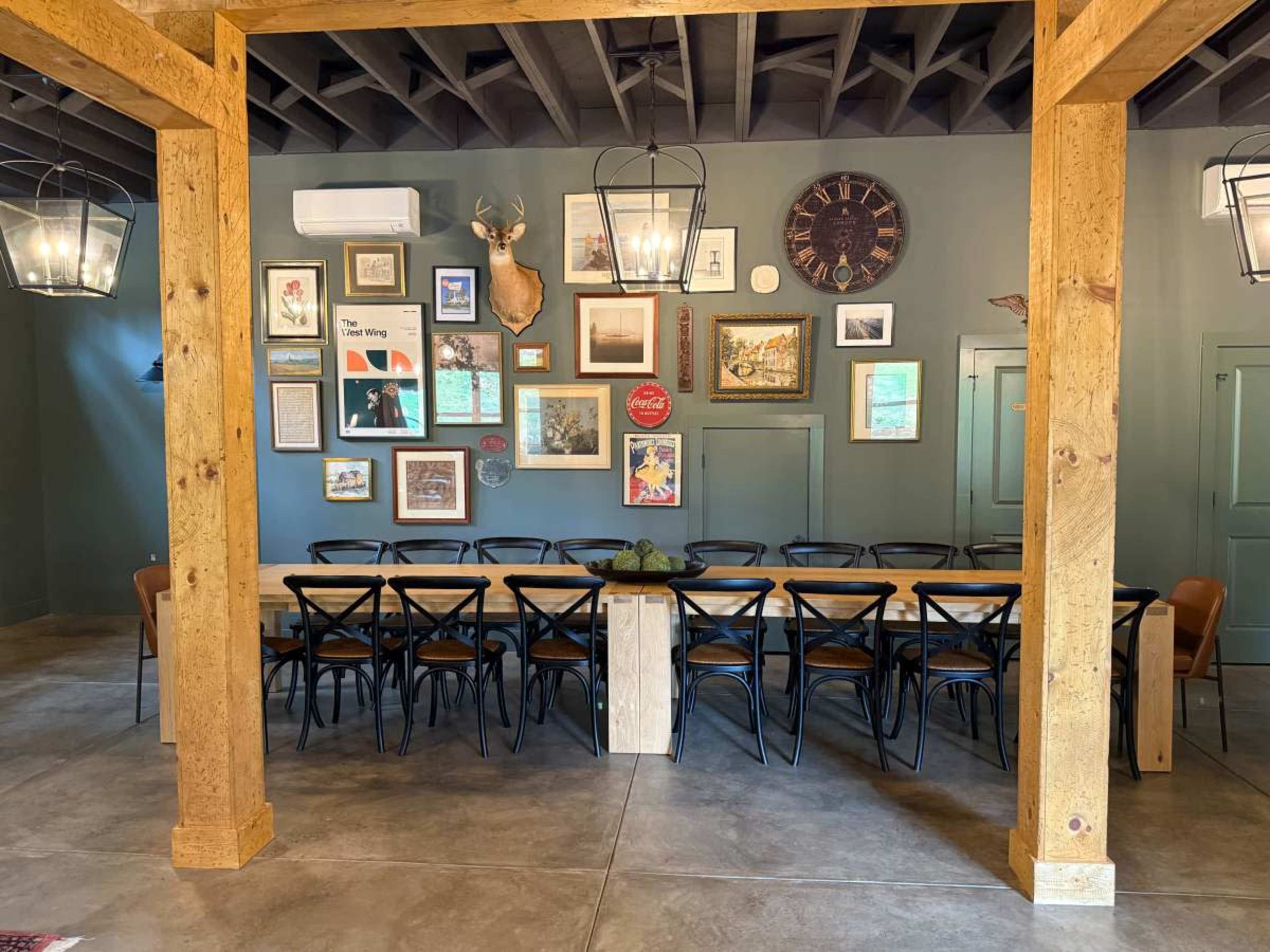 The image shows a dining area with a long wooden table surrounded by black chairs, adorned by a gallery wall of framed artwork and decorative items.