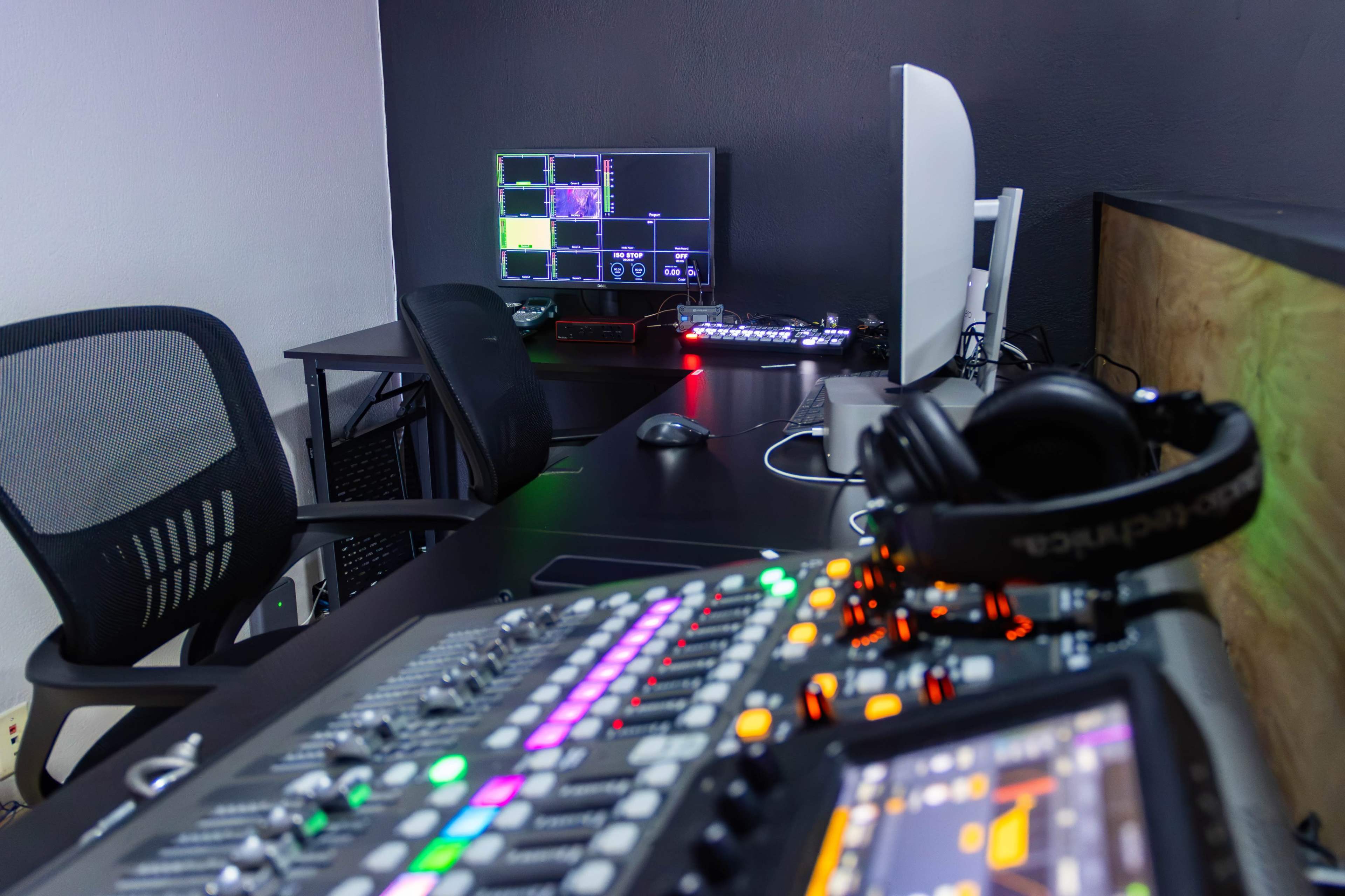 The image shows a monitoring setup with a large screen, a sound mixing console, and two office chairs in a dimly lit room.