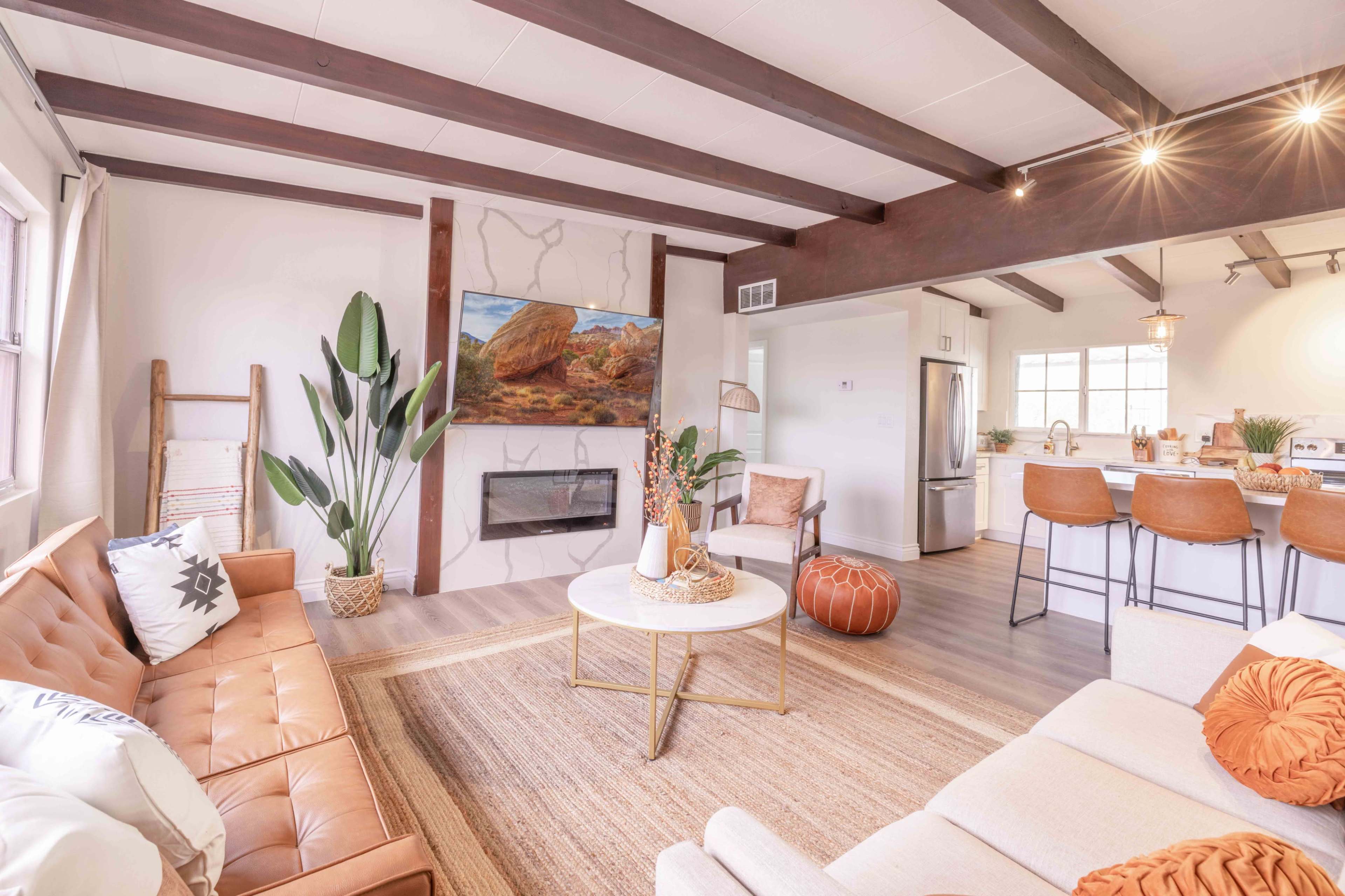 The image shows a modern living room with a tan leather sofa, a circular coffee table, and an artwork featuring a rock landscape hanging above a minimalistic fireplace.