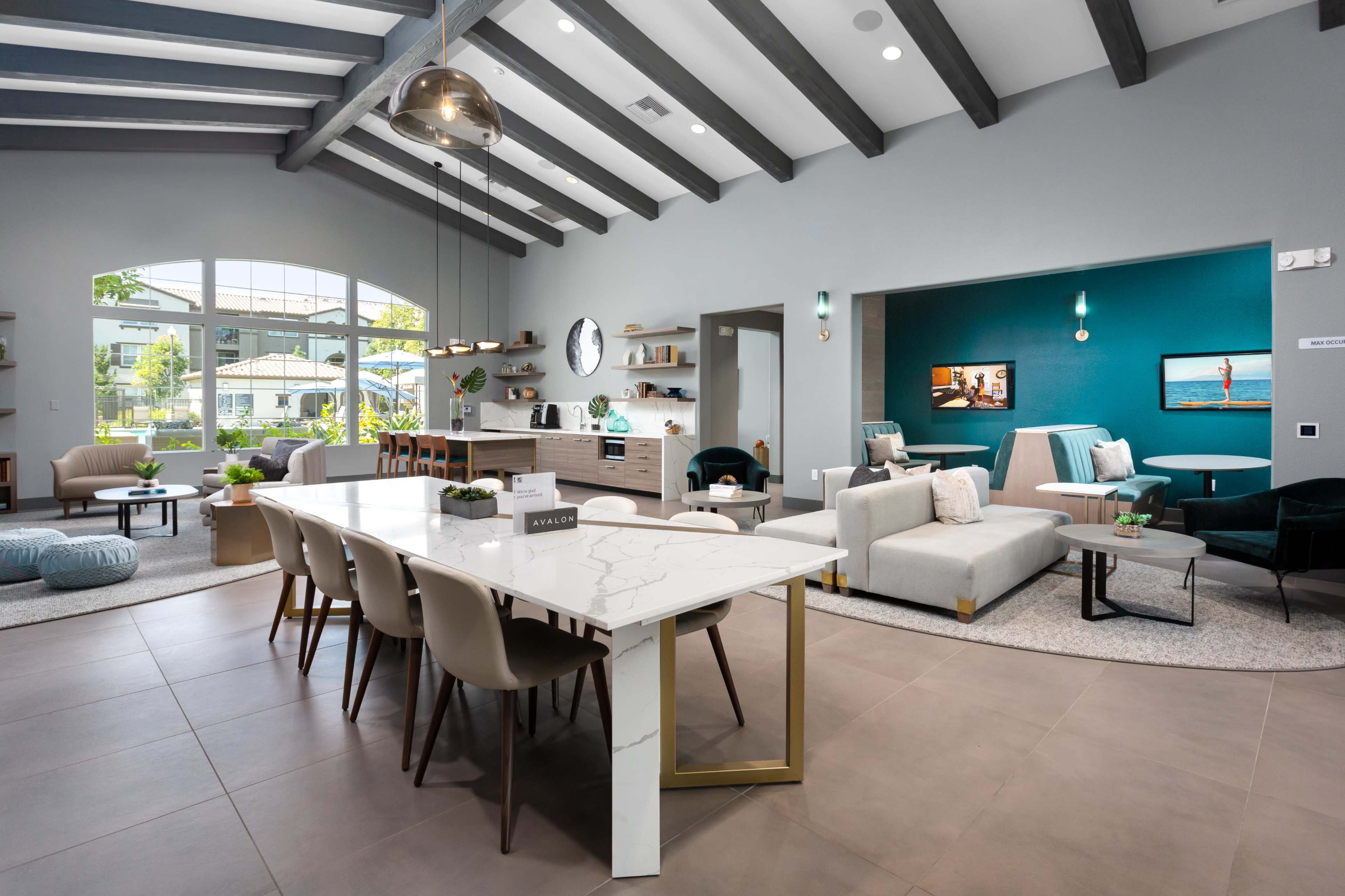 A spacious modern living area features a marble dining table, a sectional sofa, and large windows allowing natural light to illuminate the space.