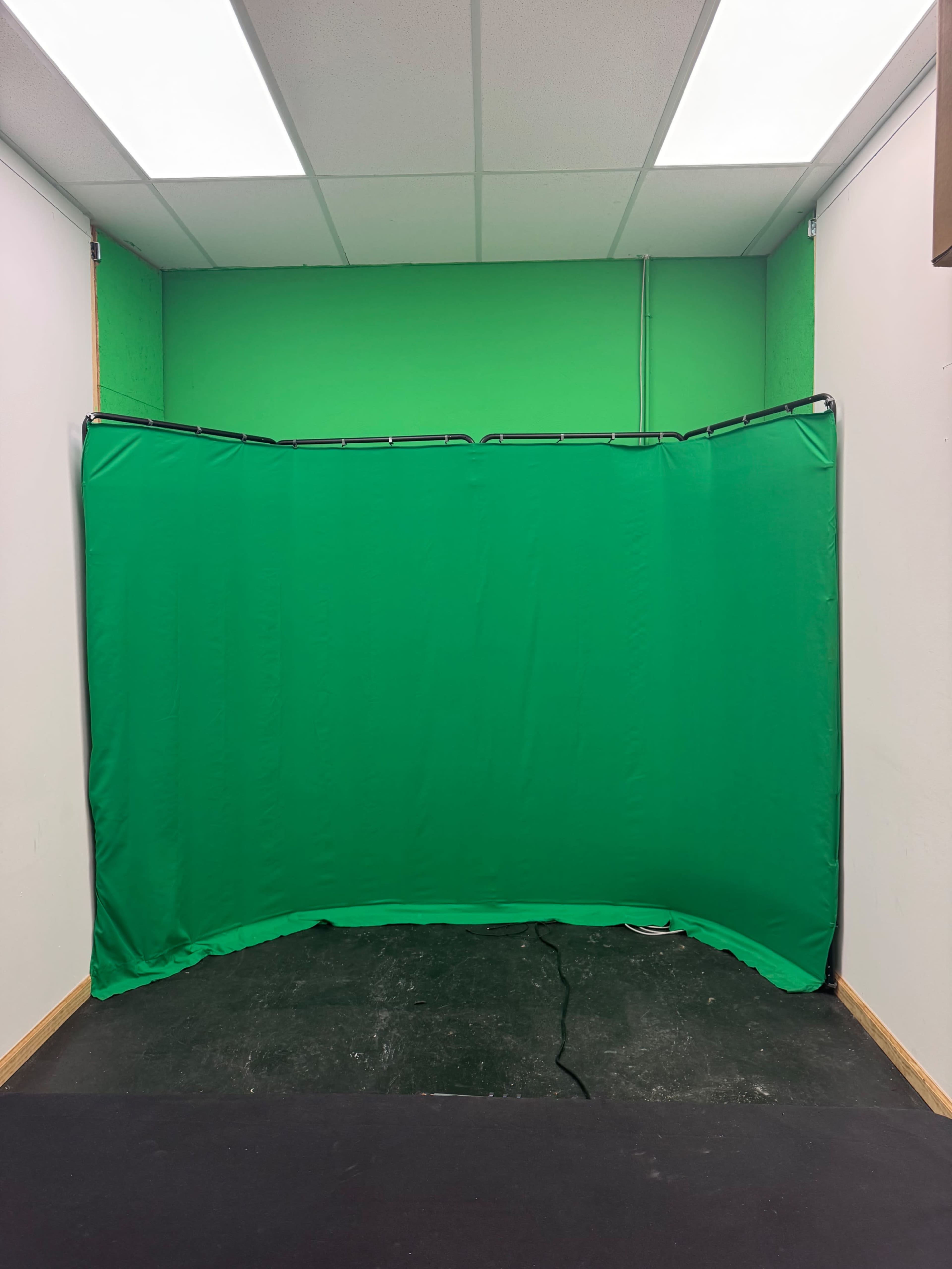 The image shows a green screen setup in a room with white walls and a flat black floor.