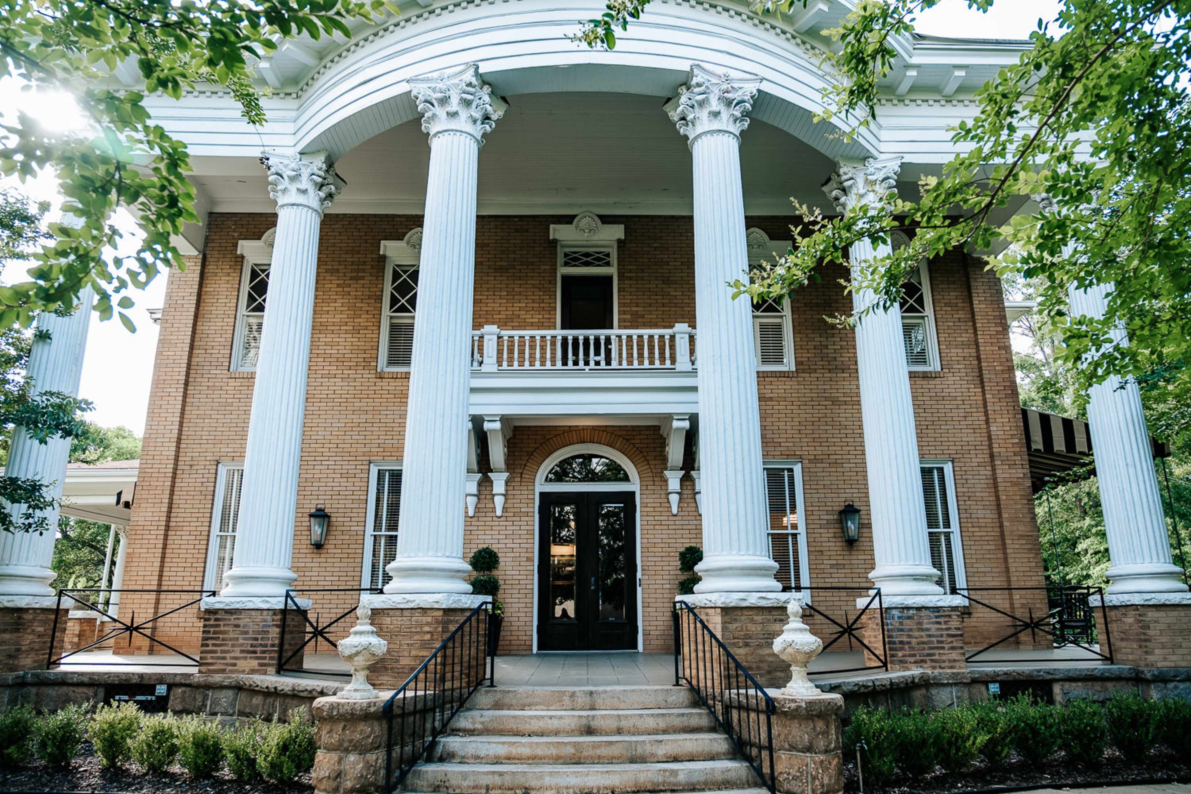 A two-story brick mansion with a grand entrance featuring tall white columns and a wide staircase.