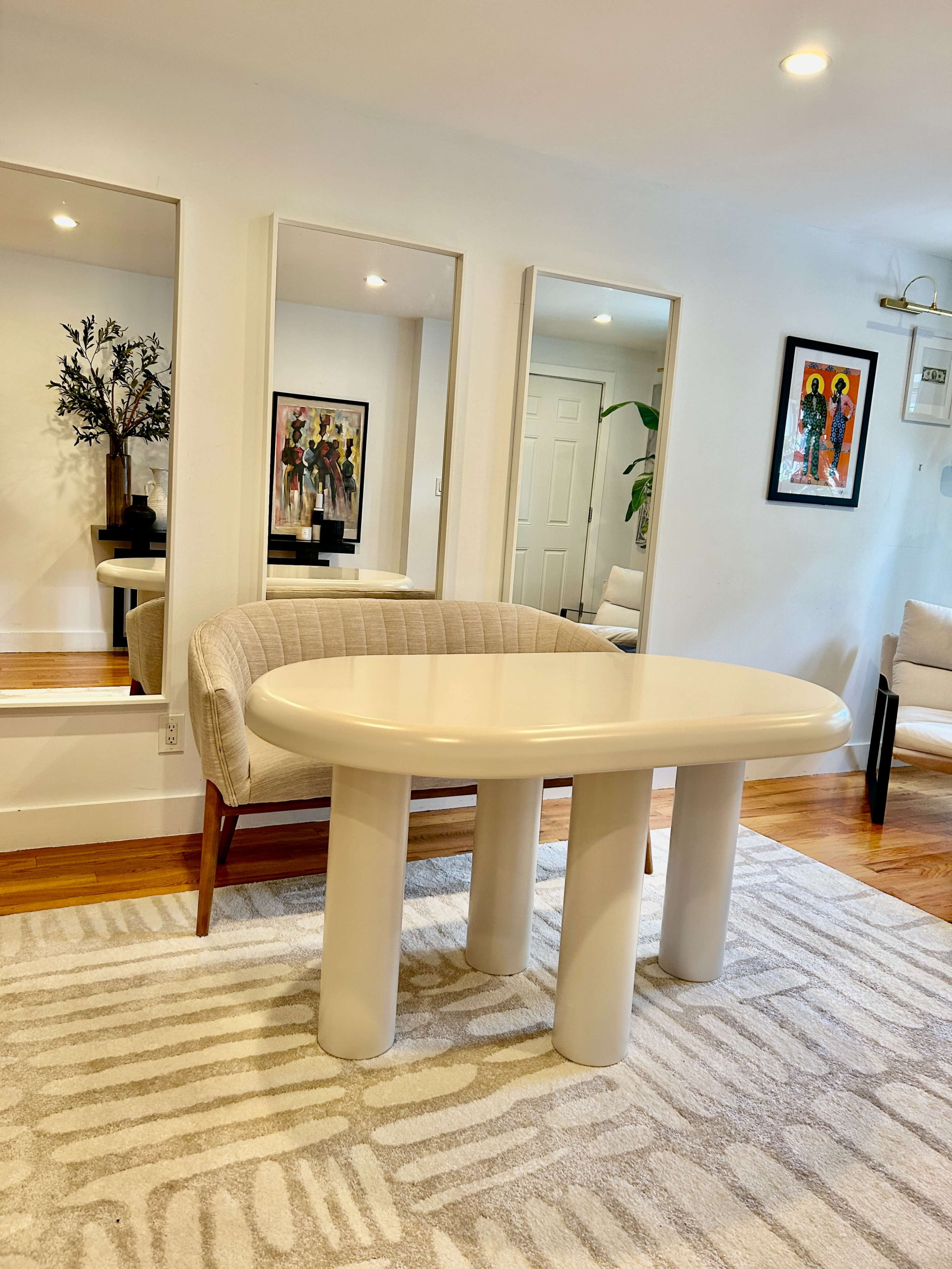 A modern living space featuring a light-colored table with four cylindrical legs, surrounded by reflective mirrors and minimalistic furniture.