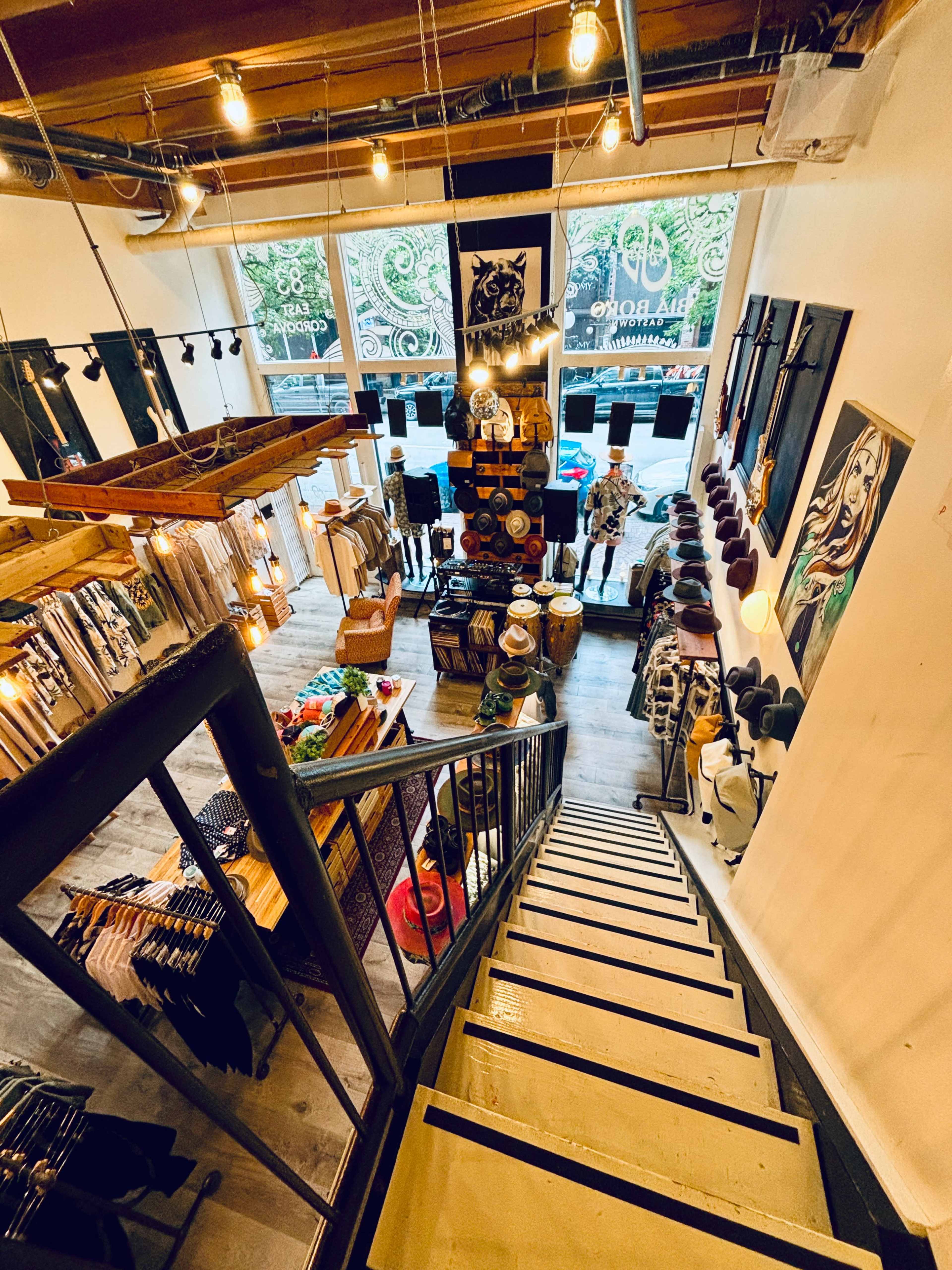 A staircase leads down to a clothing store featuring a variety of apparel, accessories, and decor displayed throughout the space.
