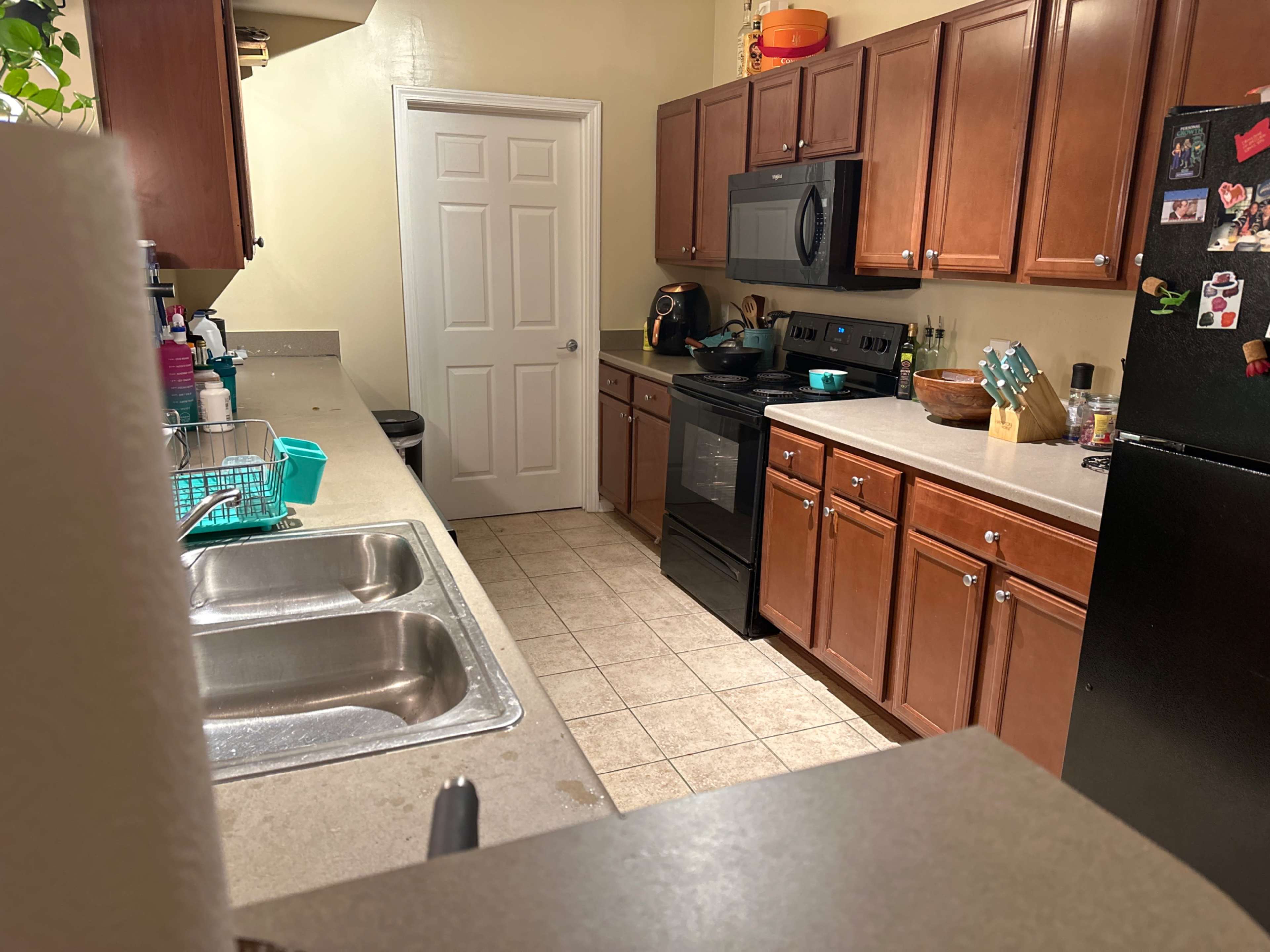 A narrow kitchen with wooden cabinets, a stove, a microwave, and a sink, along with a refrigerator on the right side.