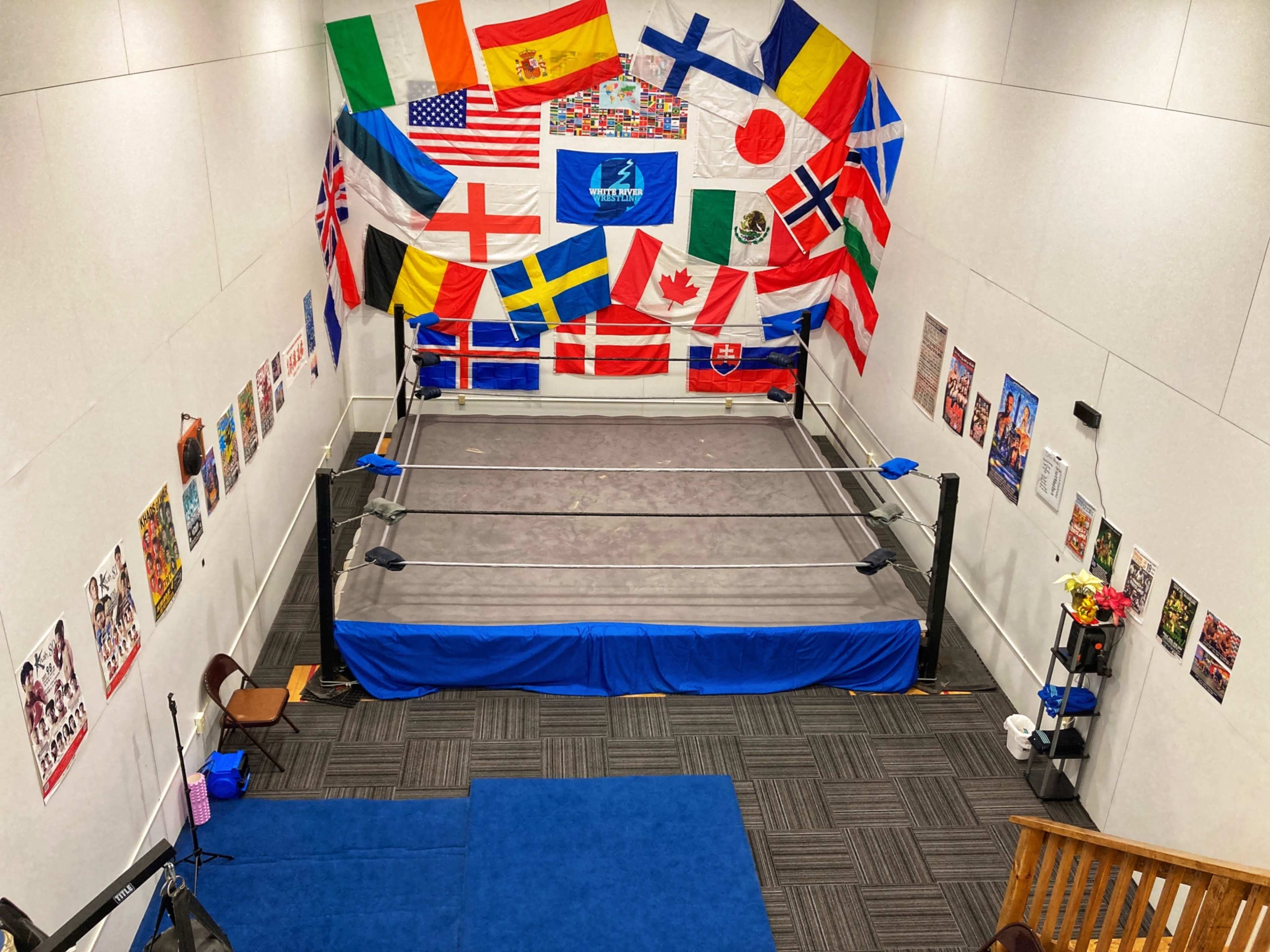A wrestling ring set up in a room decorated with flags from various countries and posters on the walls.