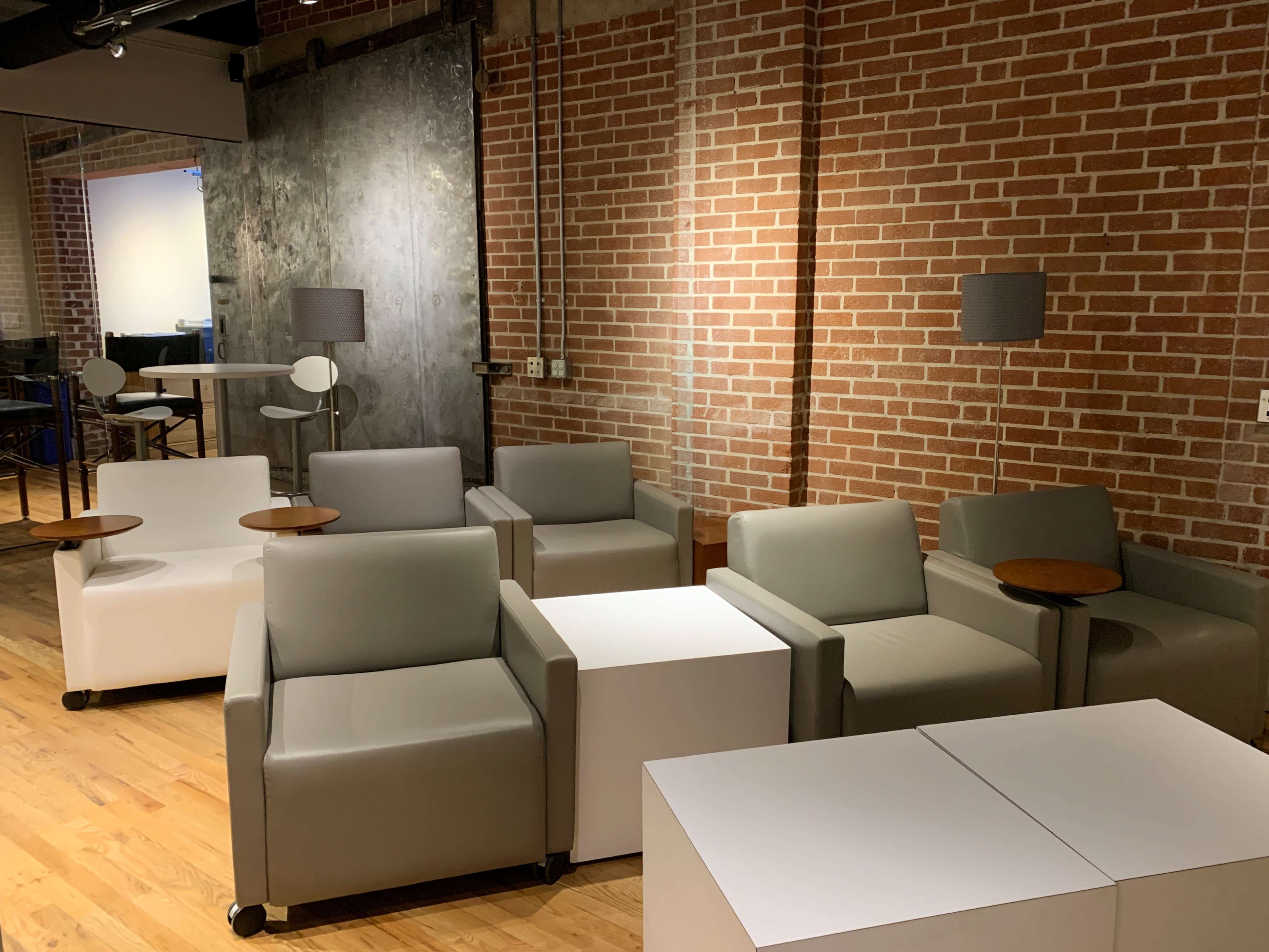A seating area with gray and white chairs, small wooden side tables, and a brick wall backdrop.