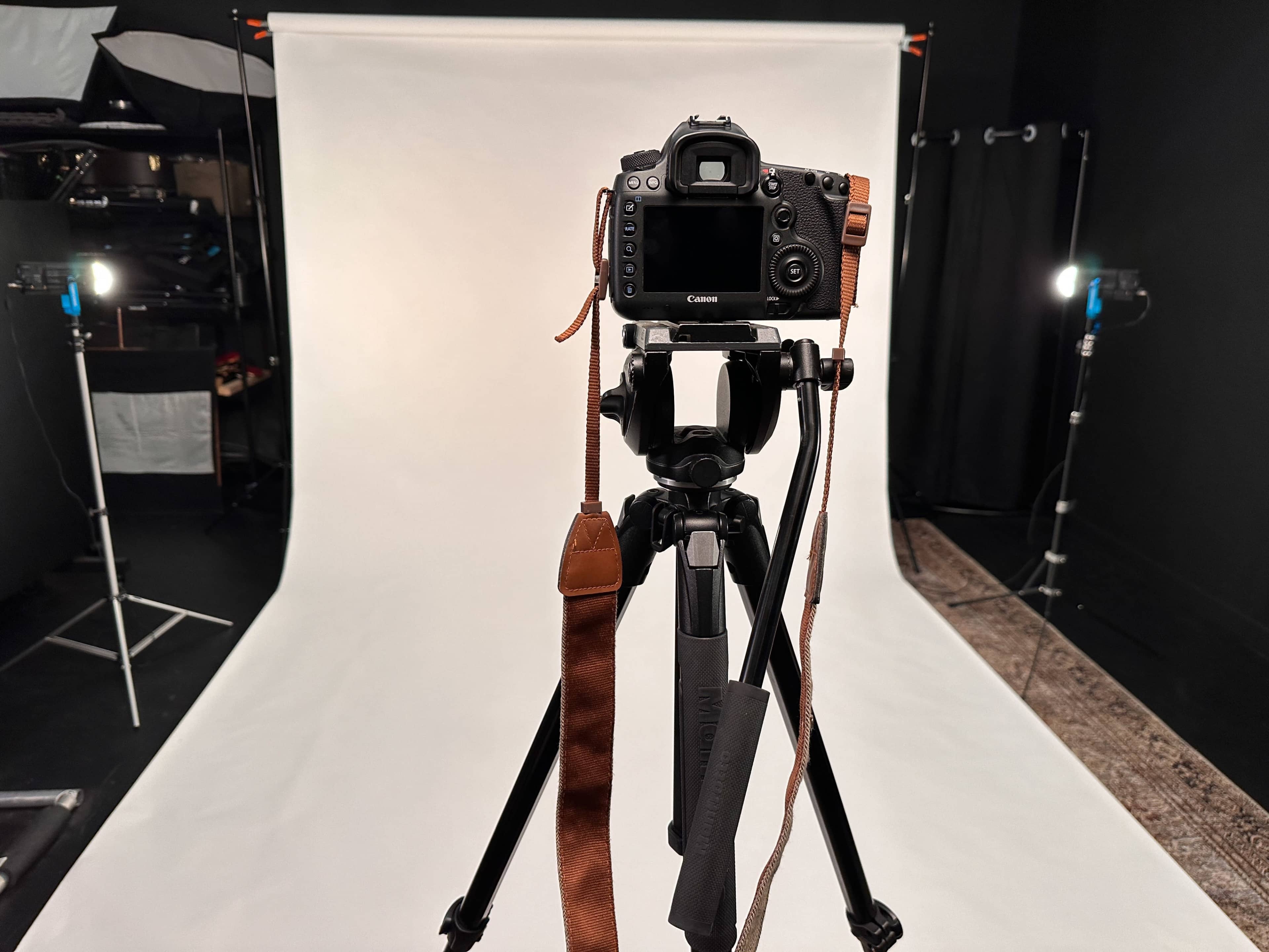 A Canon camera is mounted on a tripod in front of a plain white backdrop in a photography studio.