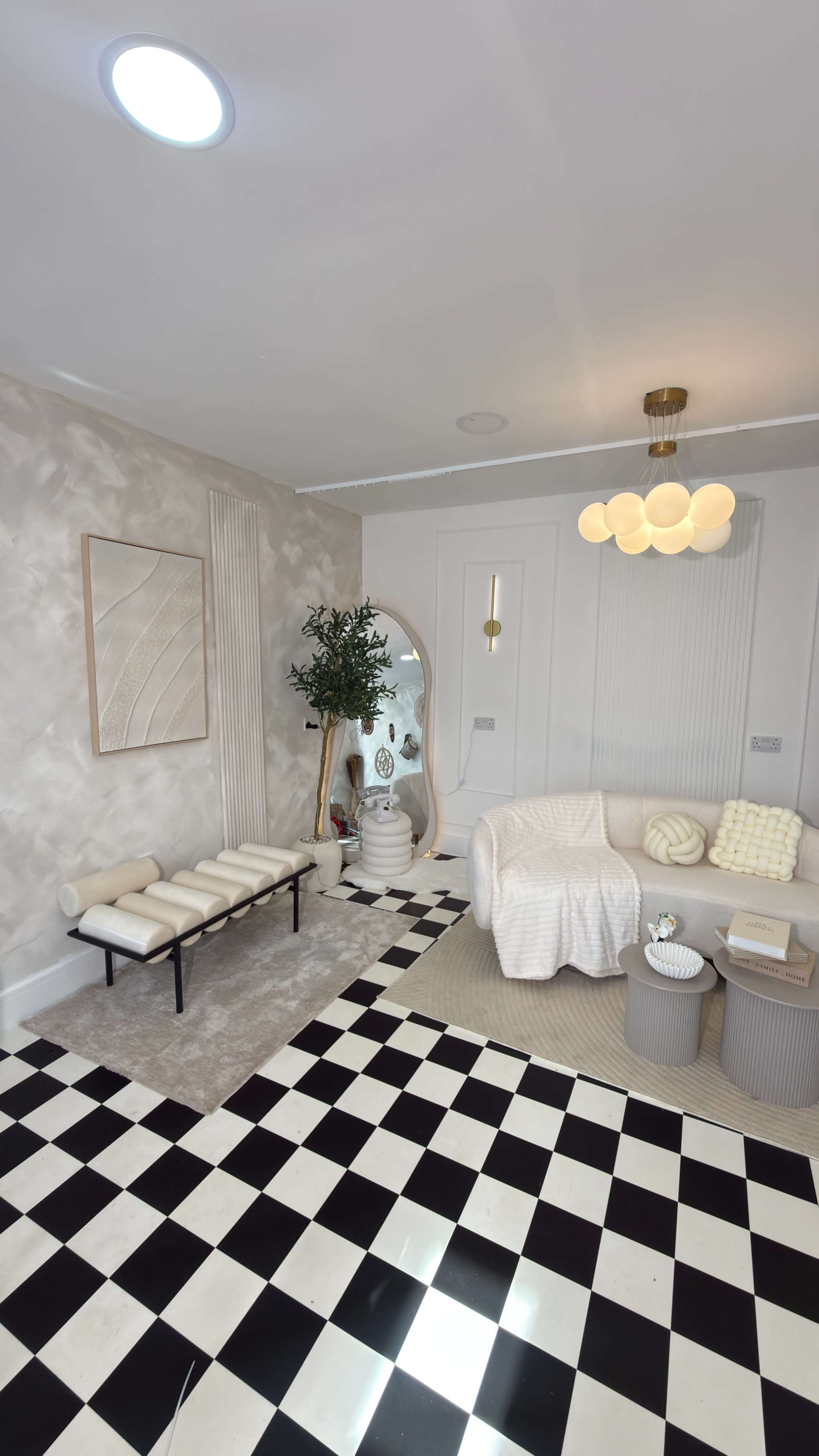 The image shows a modern, stylish living room featuring a curved white sofa, a round coffee table, and a patterned black and white tiled floor.