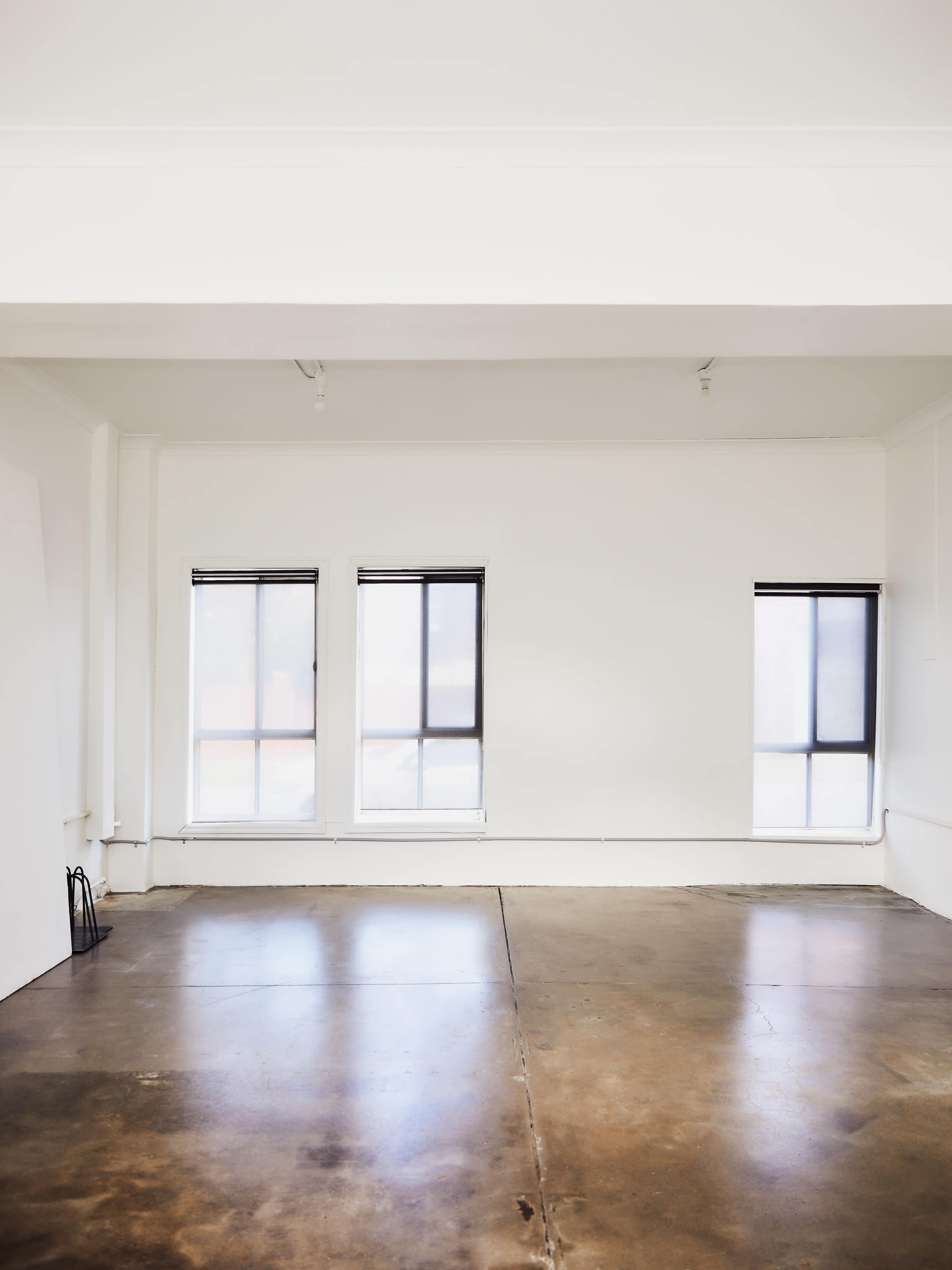 A spacious, vacant room features three large windows and a polished concrete floor.
