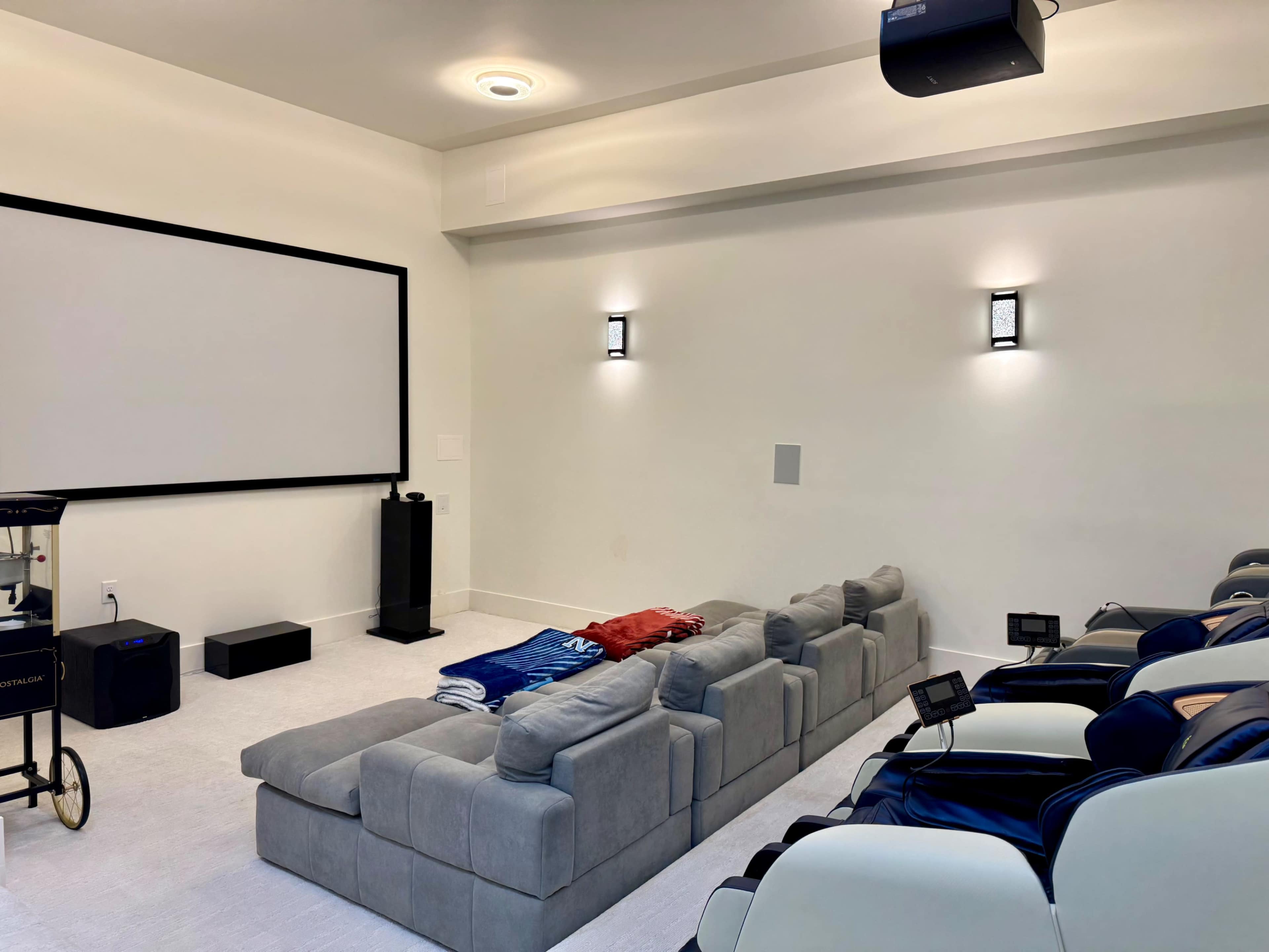 The image depicts a home theater with a large screen, a sectional sofa, and a few chairs arranged for seating.