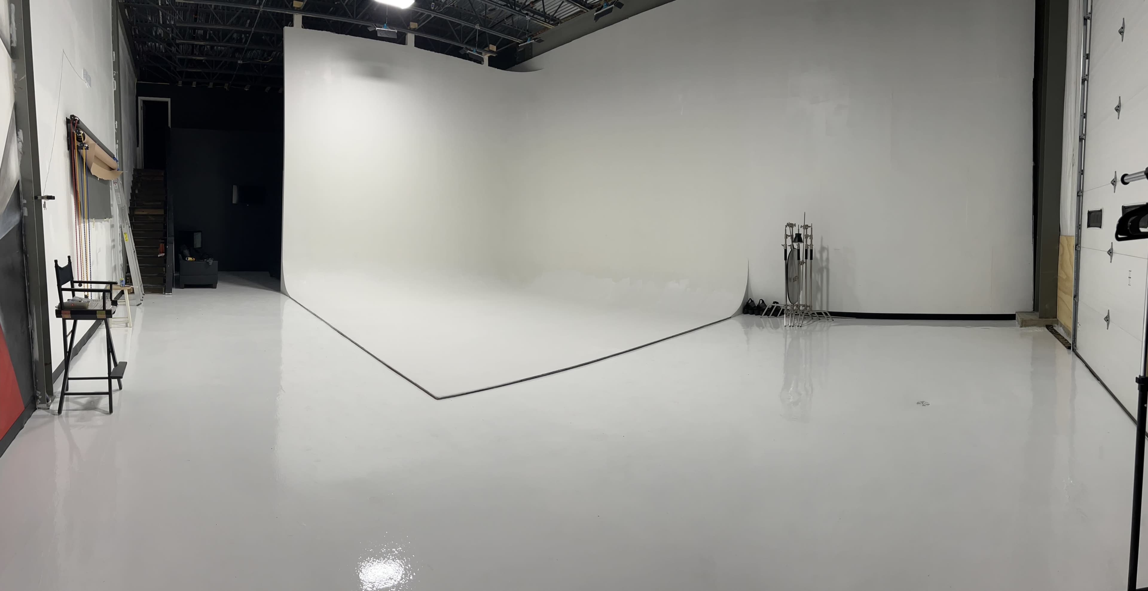 A spacious photography studio with a seamless white backdrop and polished flooring.