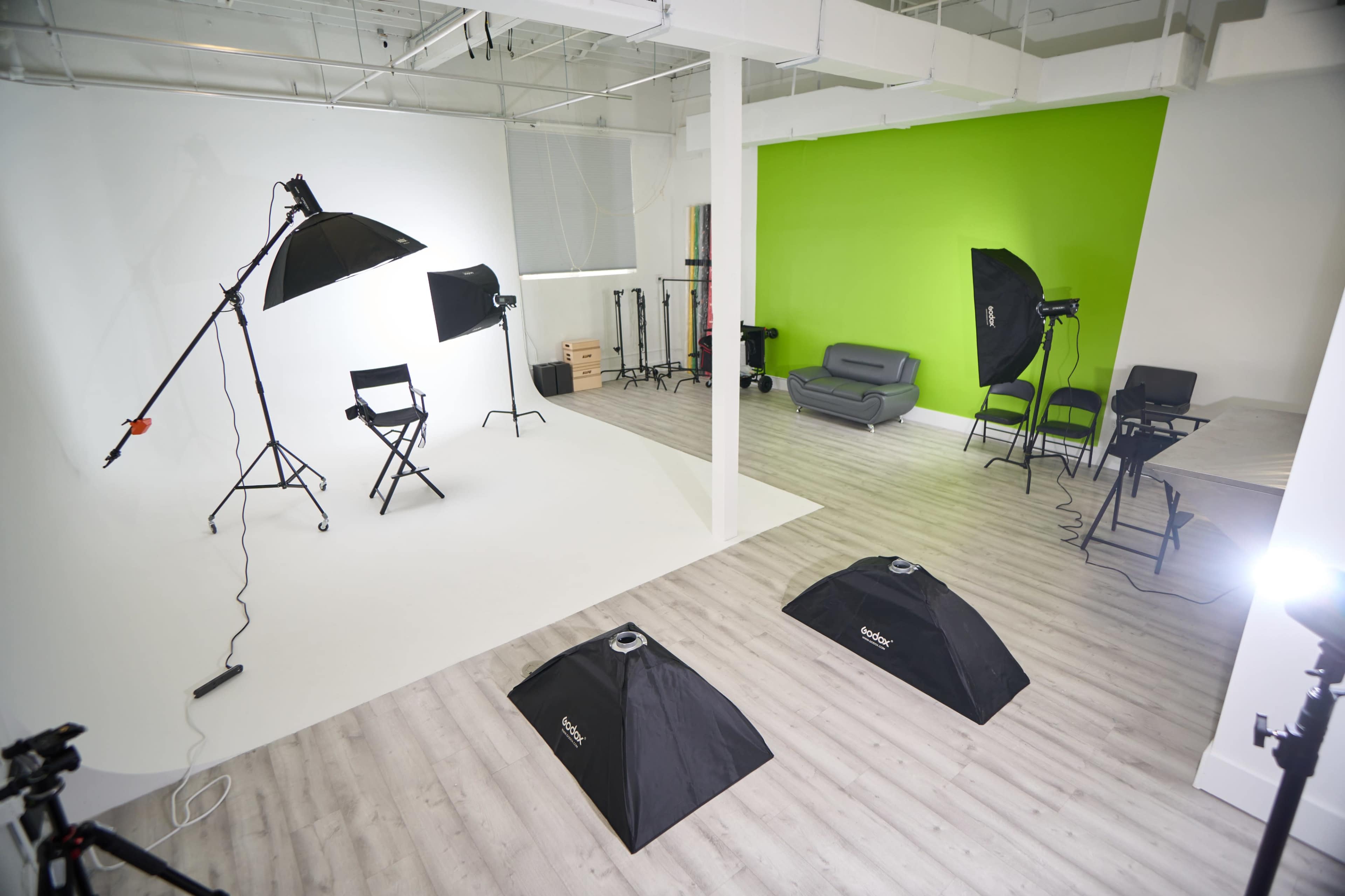 A photography studio with a white backdrop, a green wall, various lighting equipment, and seating arrangements.
