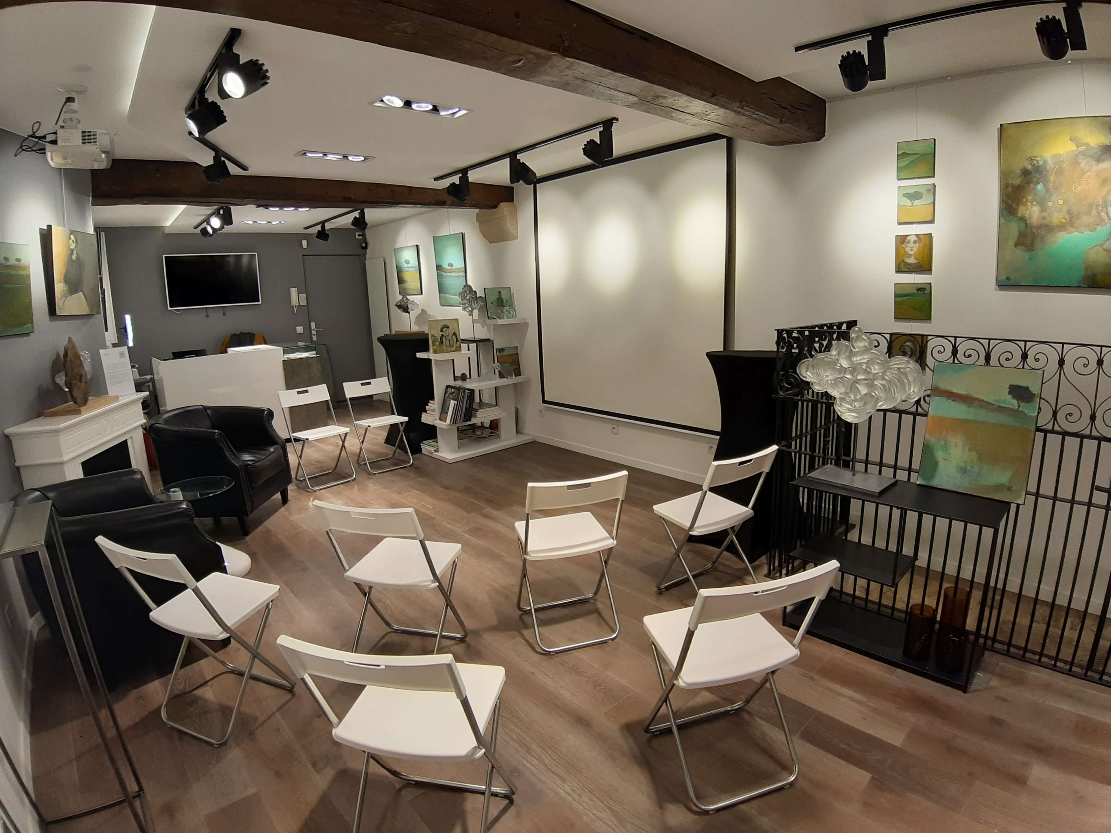 The image depicts a modern meeting room with a projector screen, seating arranged in a circle, and various artworks displayed on the walls.