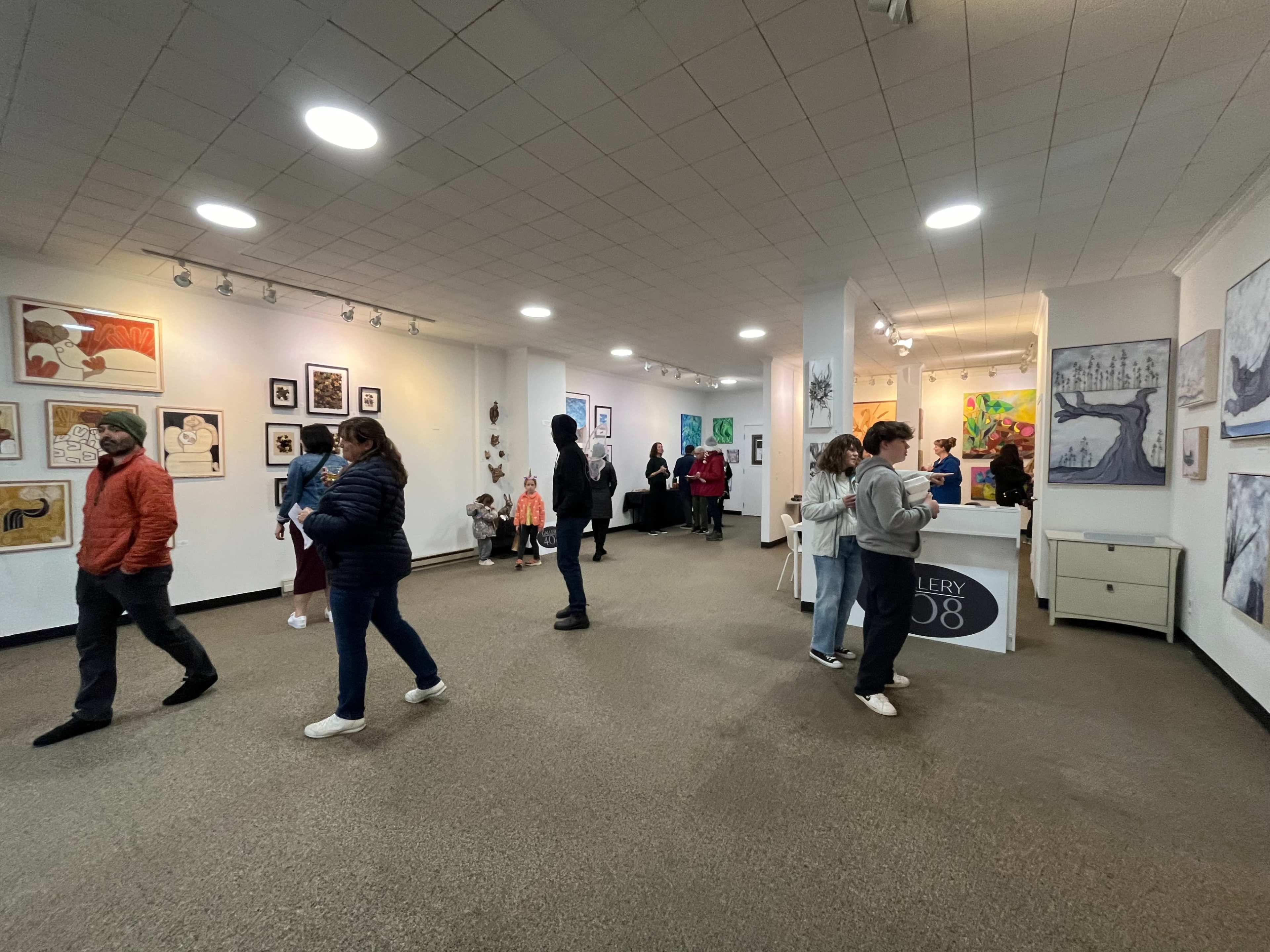 Several visitors are walking through an art gallery featuring various framed artworks on the walls.