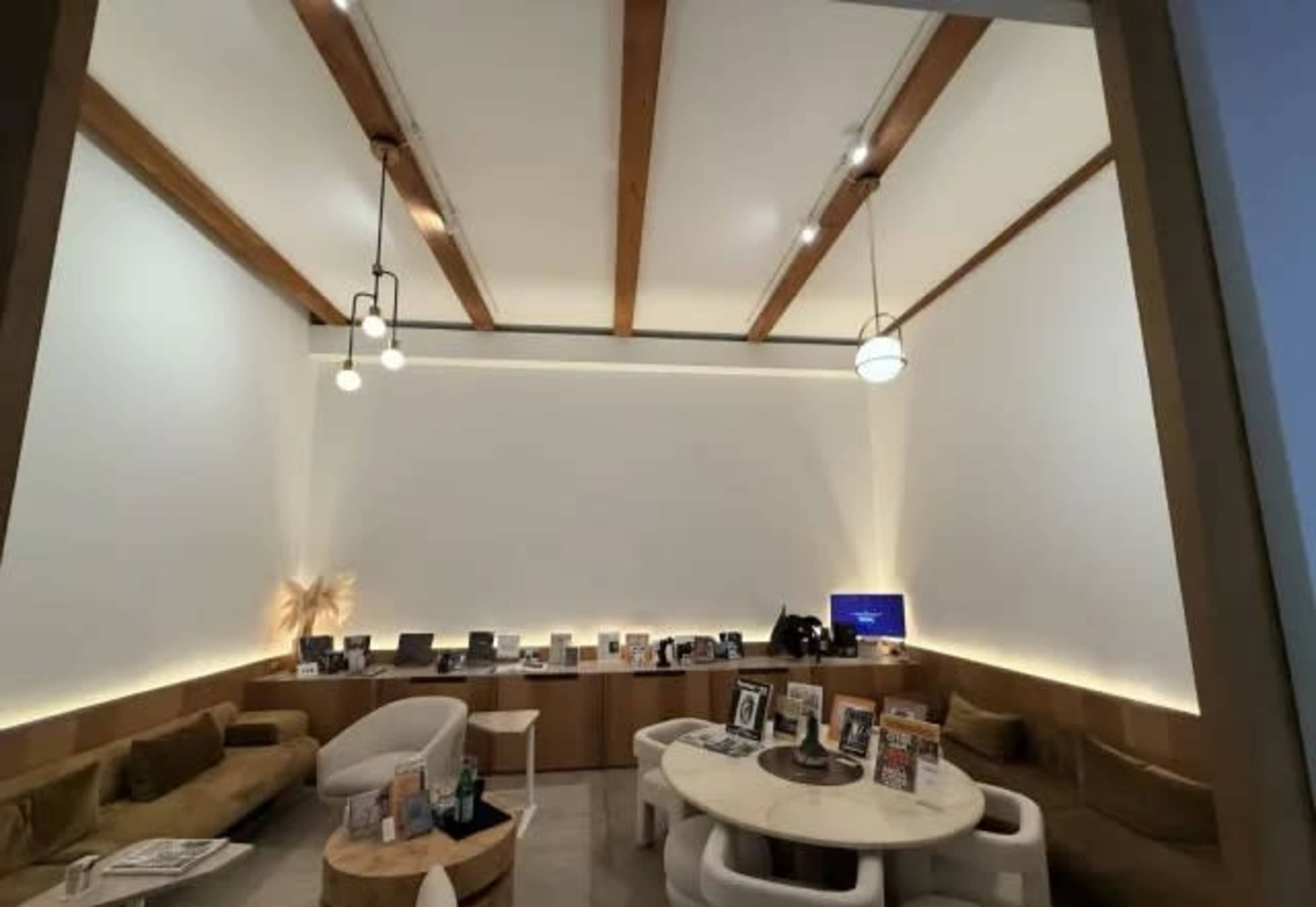 The image depicts a modern, well-lit interior lounge area featuring a circular table, chairs, and decorative elements along the walls.