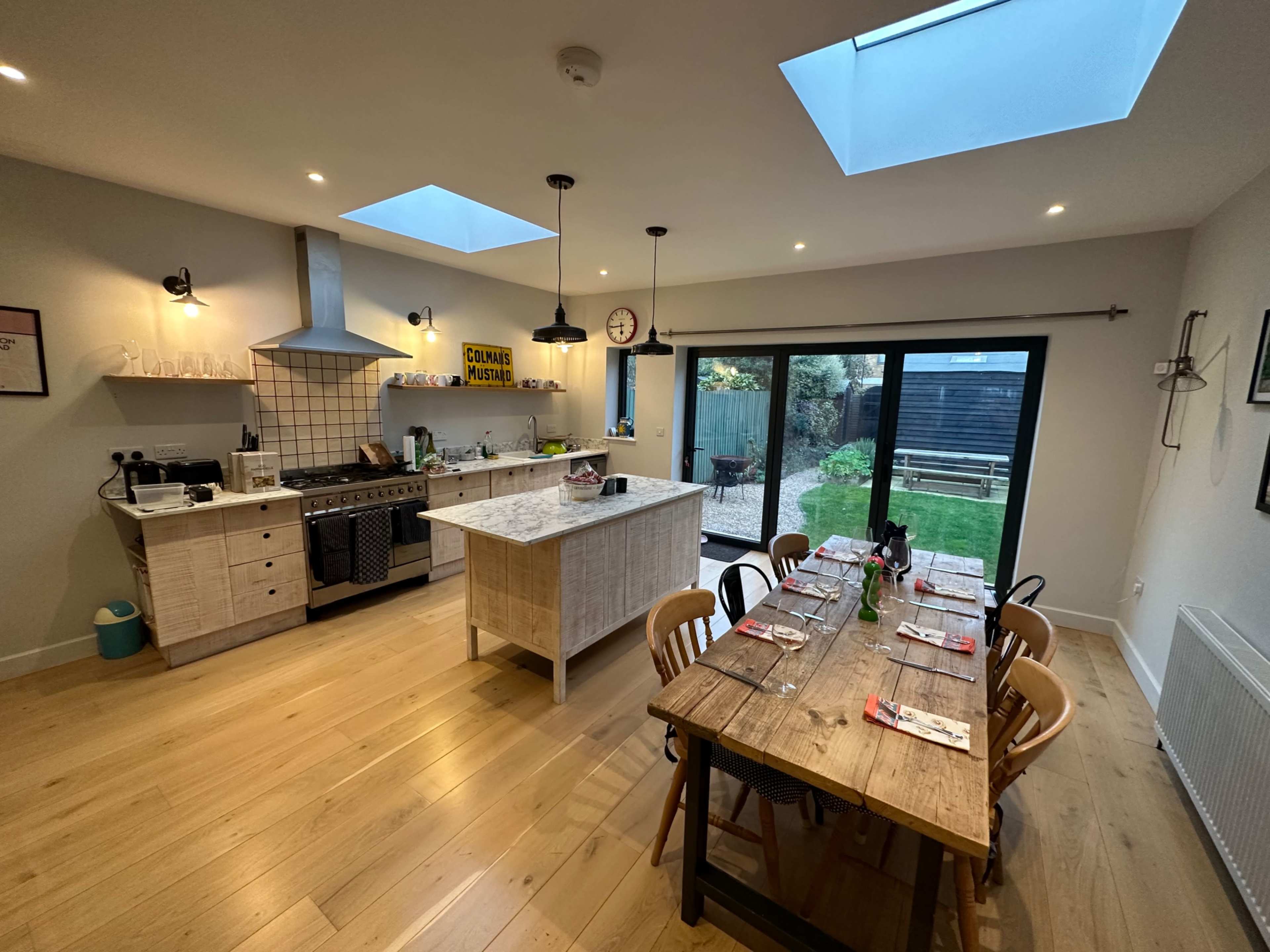 A modern kitchen features a large island, a dining table set for a meal, and skylights that illuminate the space.