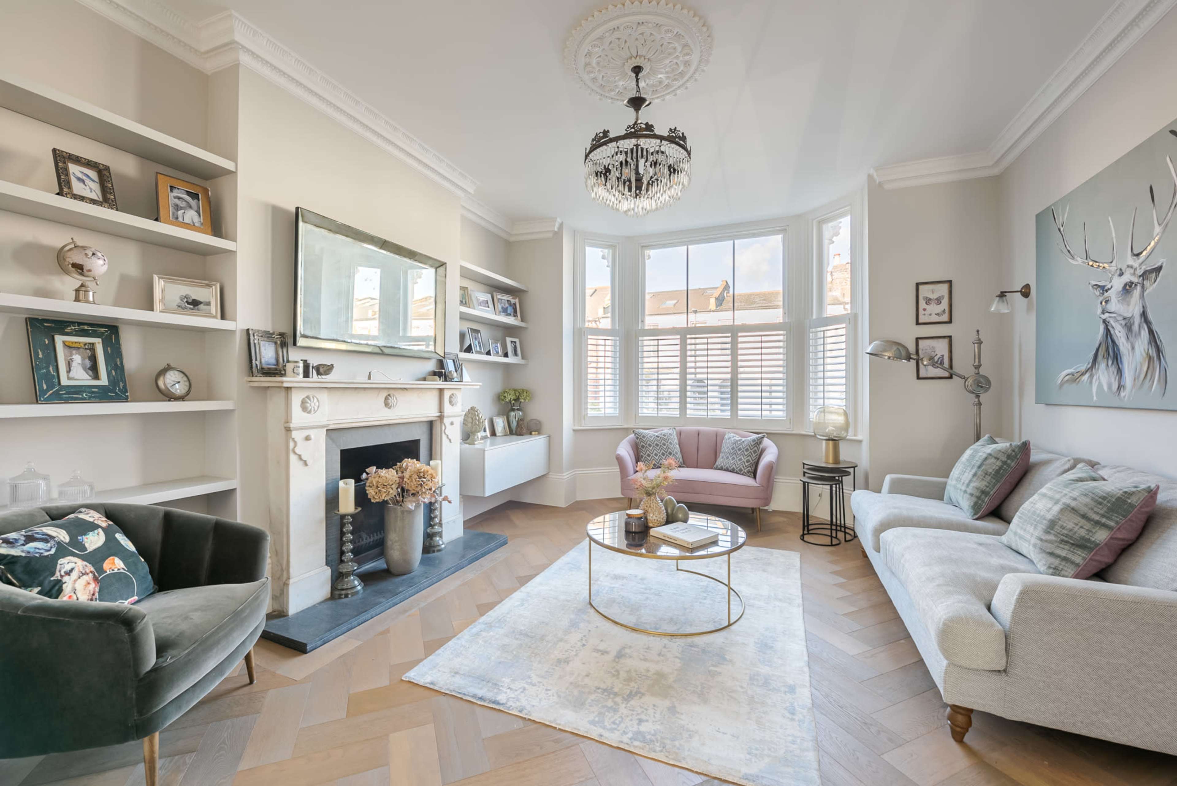 The image shows a well-lit living room featuring a fireplace, a round coffee table, and two seating areas with a mix of decorative elements on the shelves.