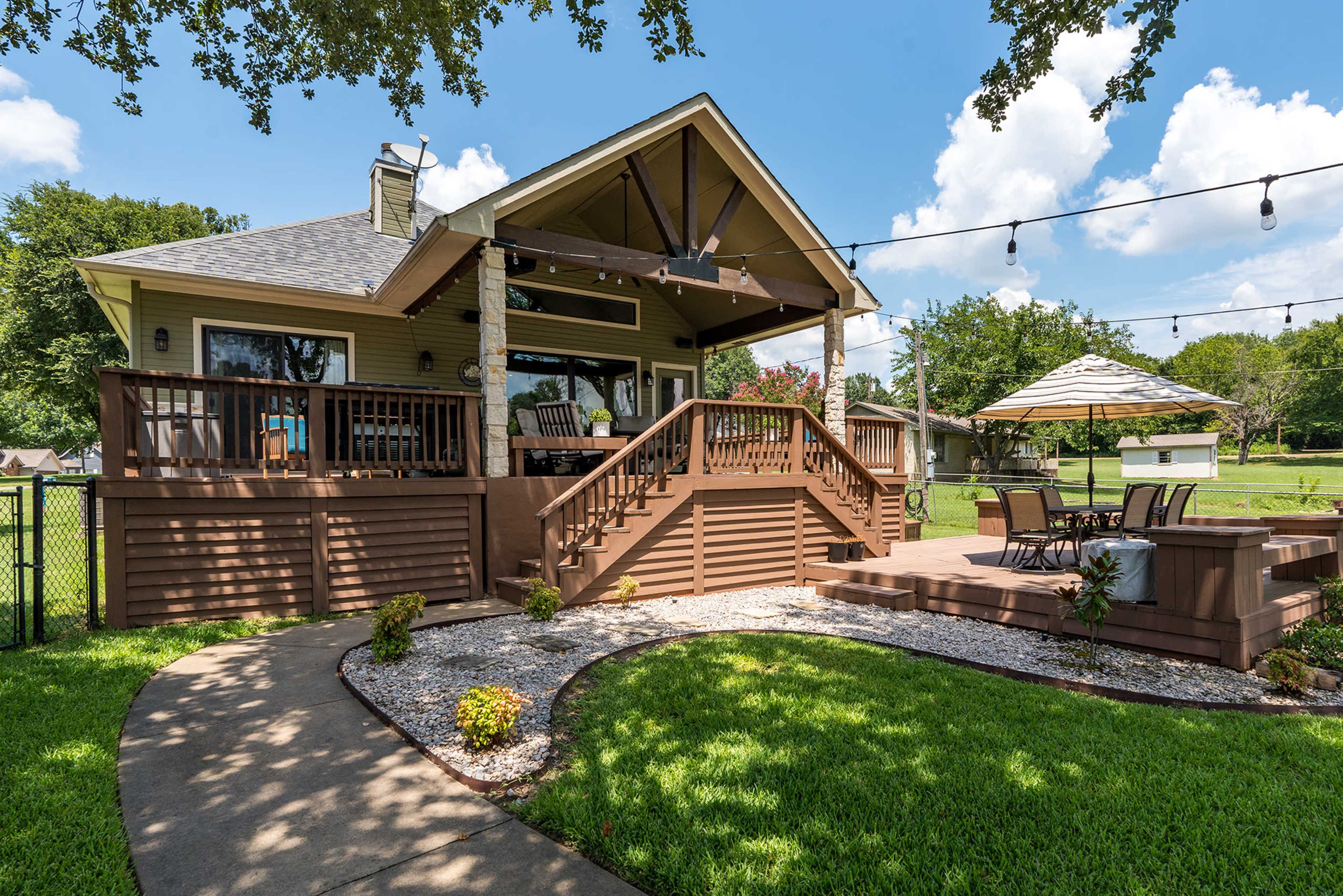 A two-story house with a front porch, surrounded by a landscaped yard and patio area featuring a table and umbrella.