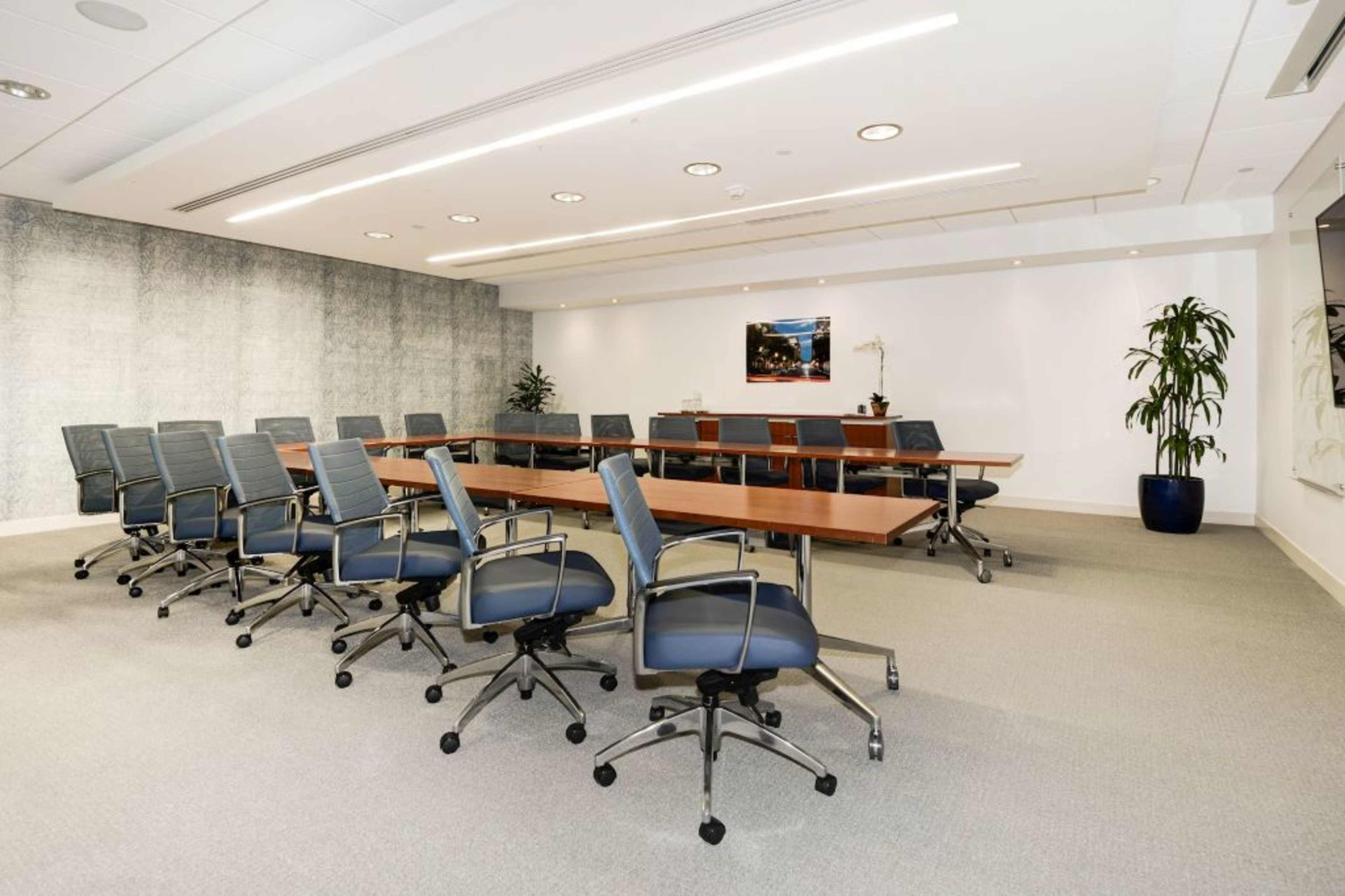 A spacious conference room is furnished with a long wooden table surrounded by ergonomic chairs and features a large wall-mounted artwork.