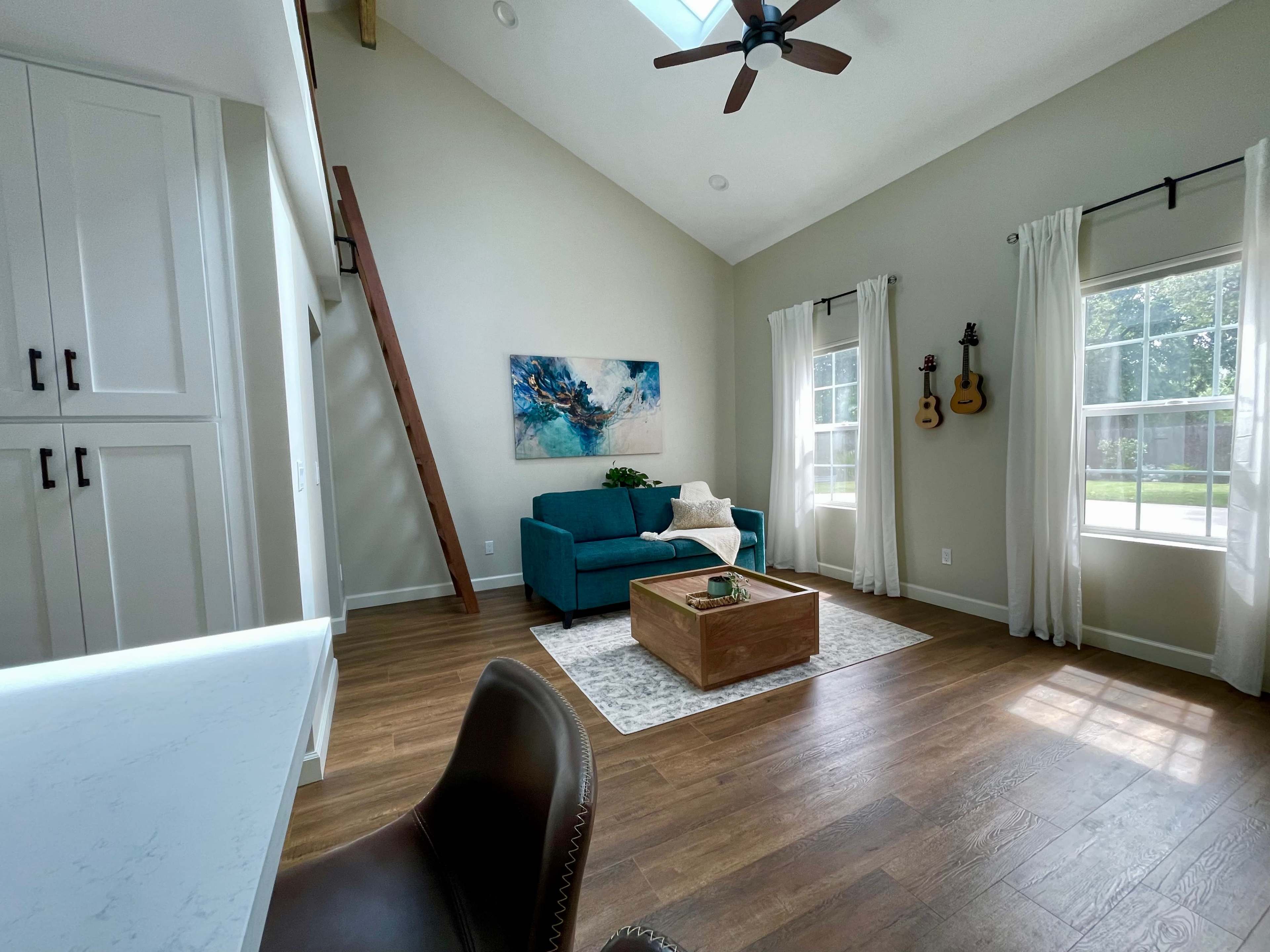 A bright, modern living room featuring a teal couch, a wooden coffee table, and a large window with natural light streaming in.