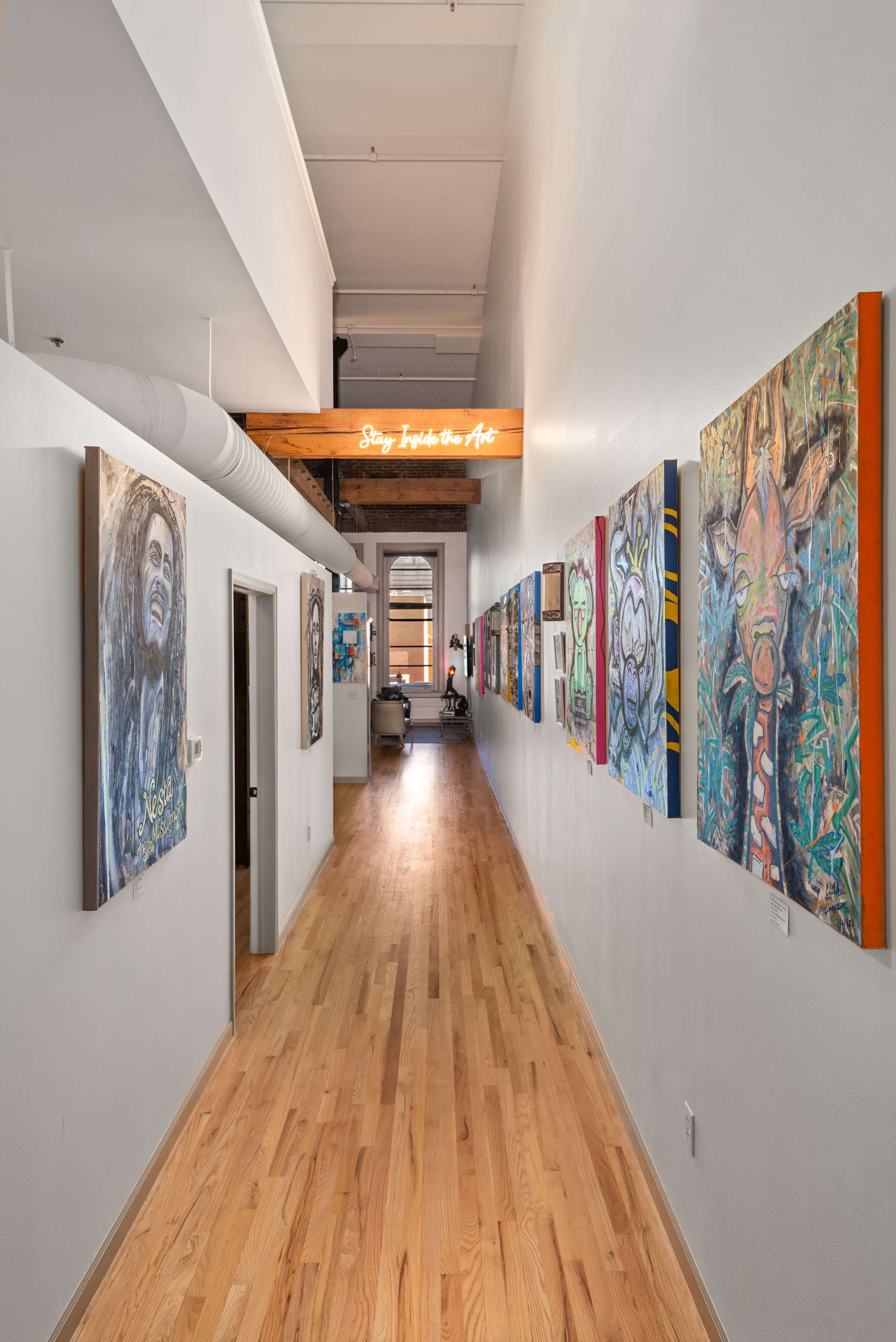 The image shows a long hallway lined with colorful artwork on the walls, leading to an open space with a visible seat at the end.