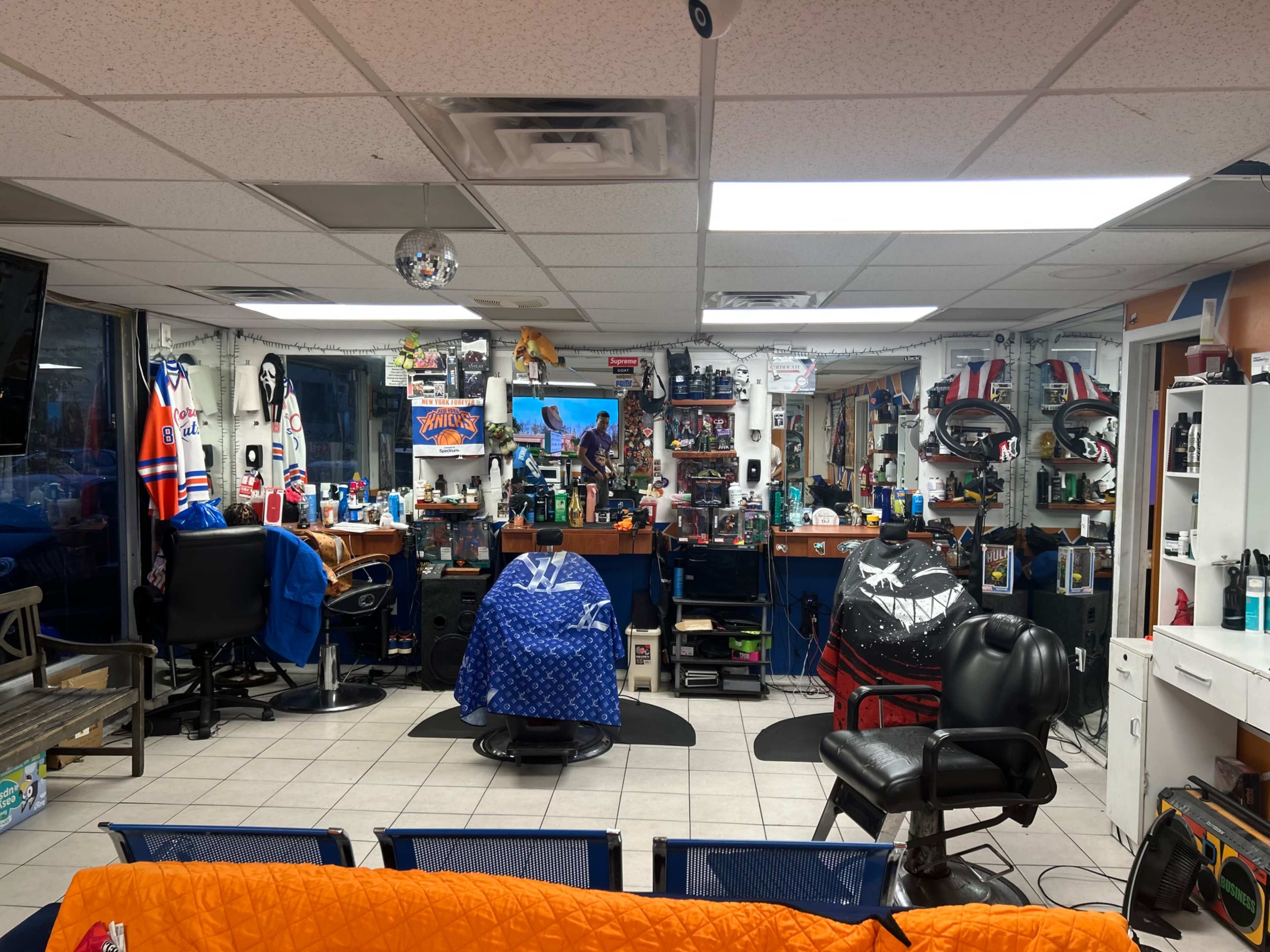 The interior of a barbershop features multiple styling stations, barbershop chairs, and various grooming products displayed on shelves.