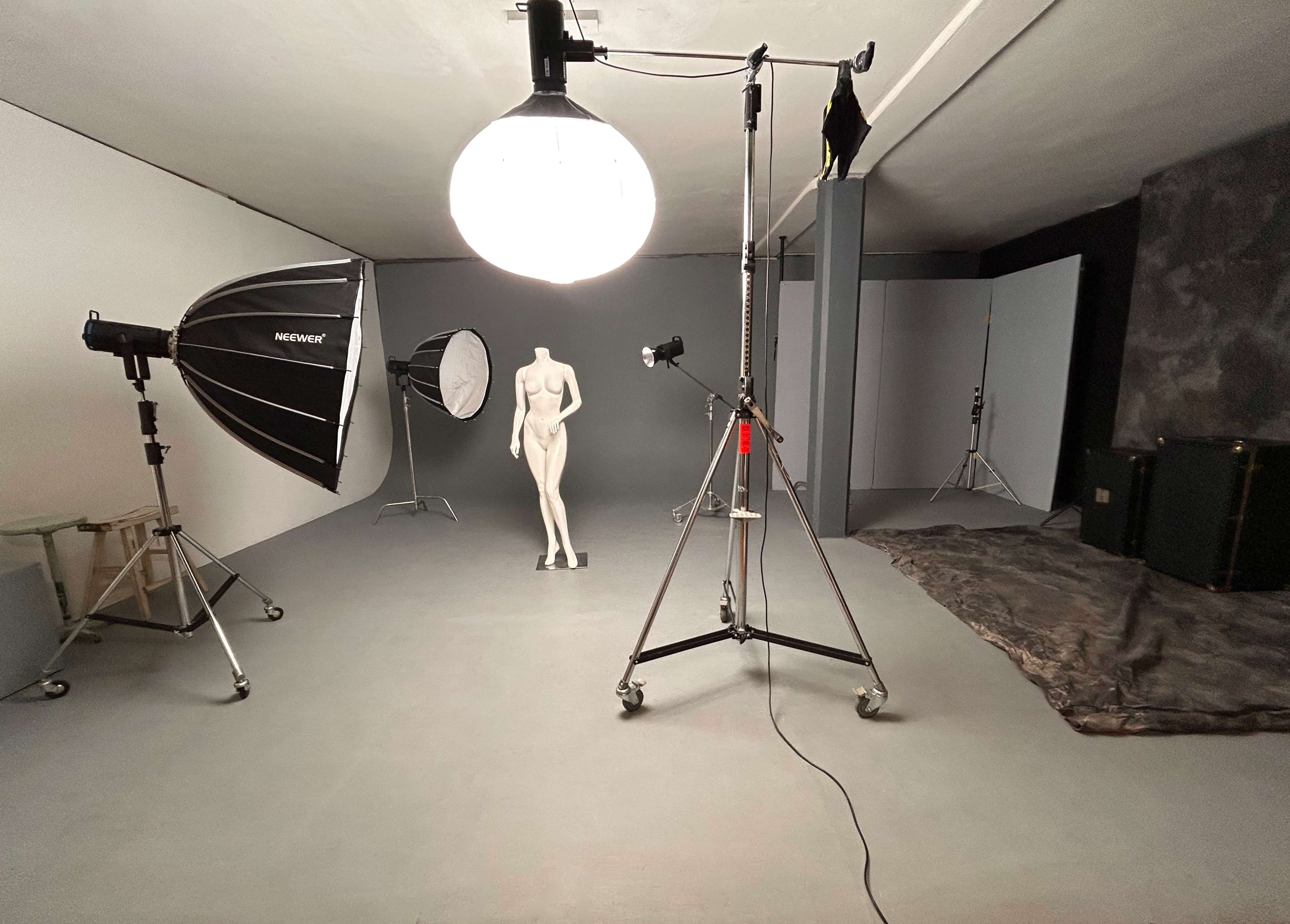 The image shows a photography studio setup with lighting equipment, a mannequin, and various backdrops.