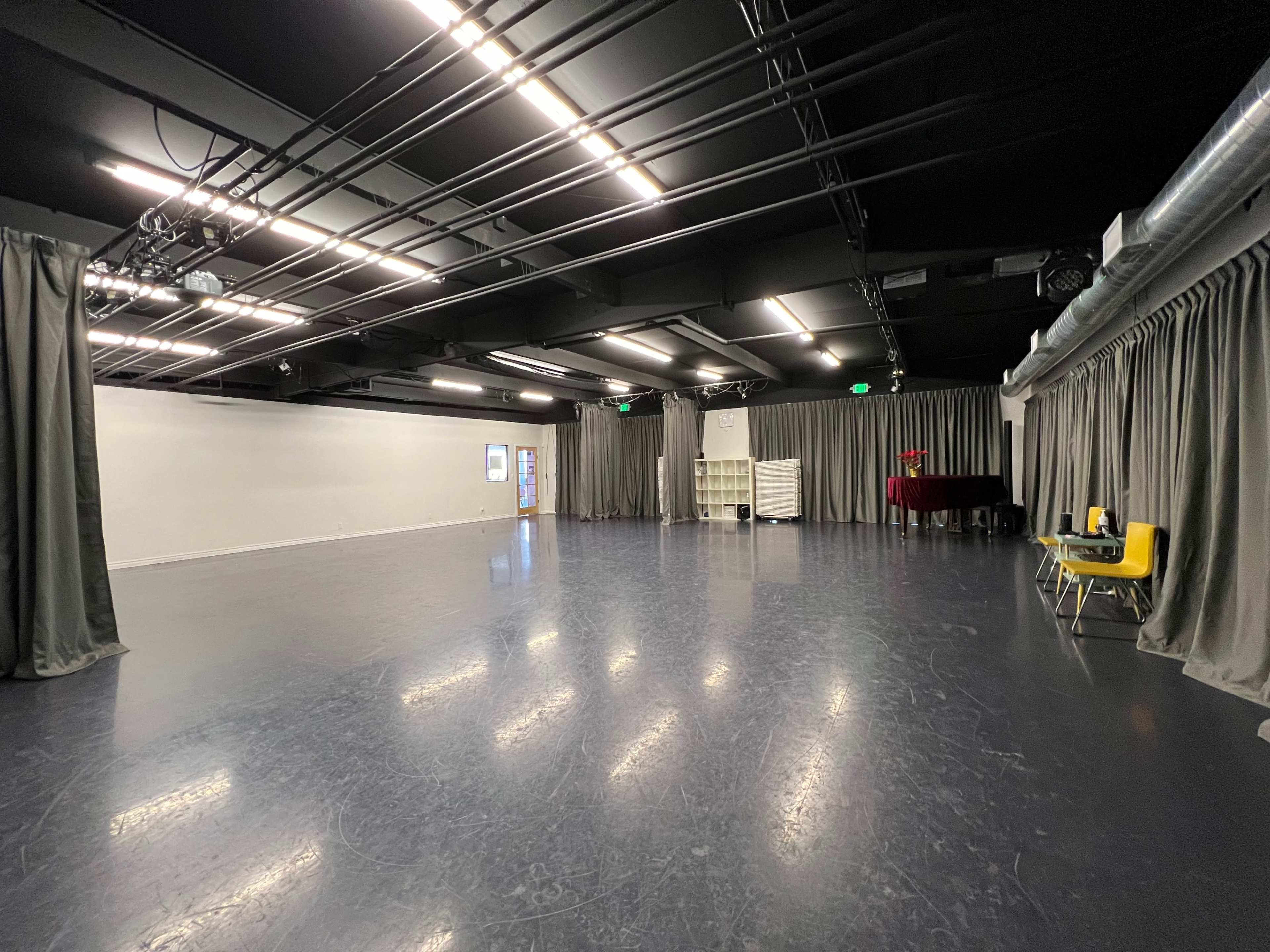 The image shows an empty studio space with gray curtains, a black floor, and a piano in the corner.