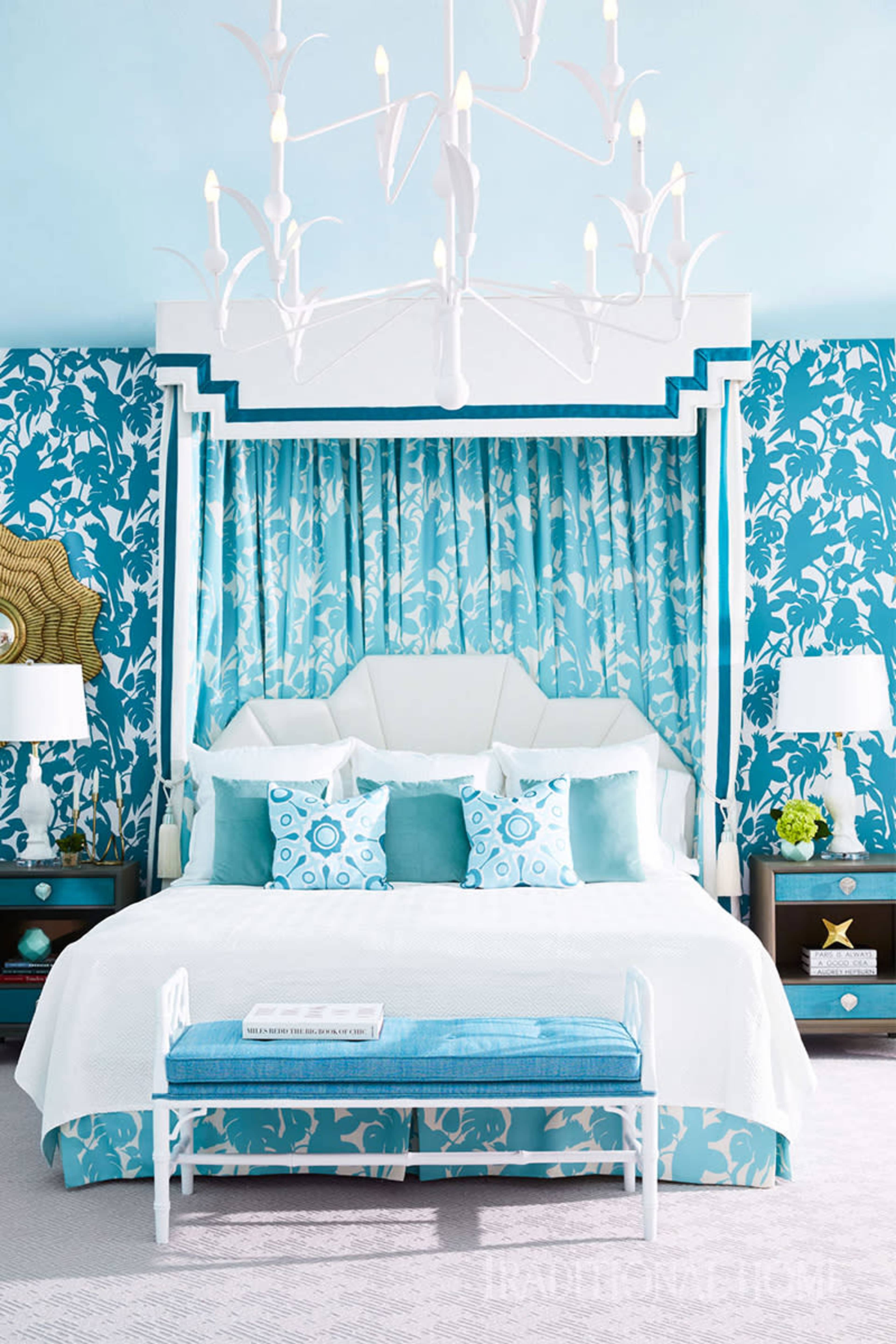 A bright bedroom with a large bed draped in turquoise and white fabric, accented by matching pillows and a decorative bench at the foot.