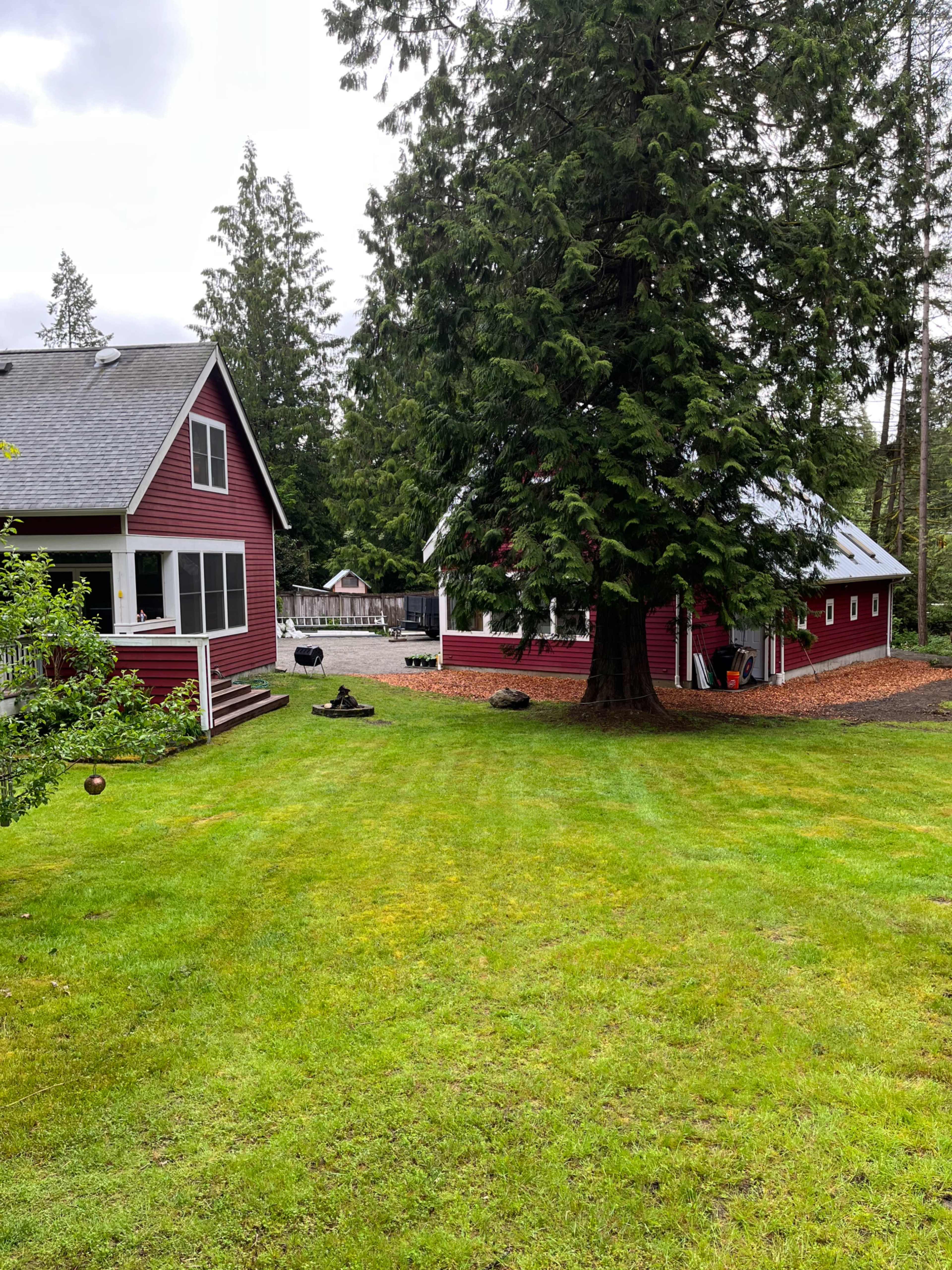 The image shows a green lawn surrounded by two red buildings, one a house and the other a barn, with trees in the background.