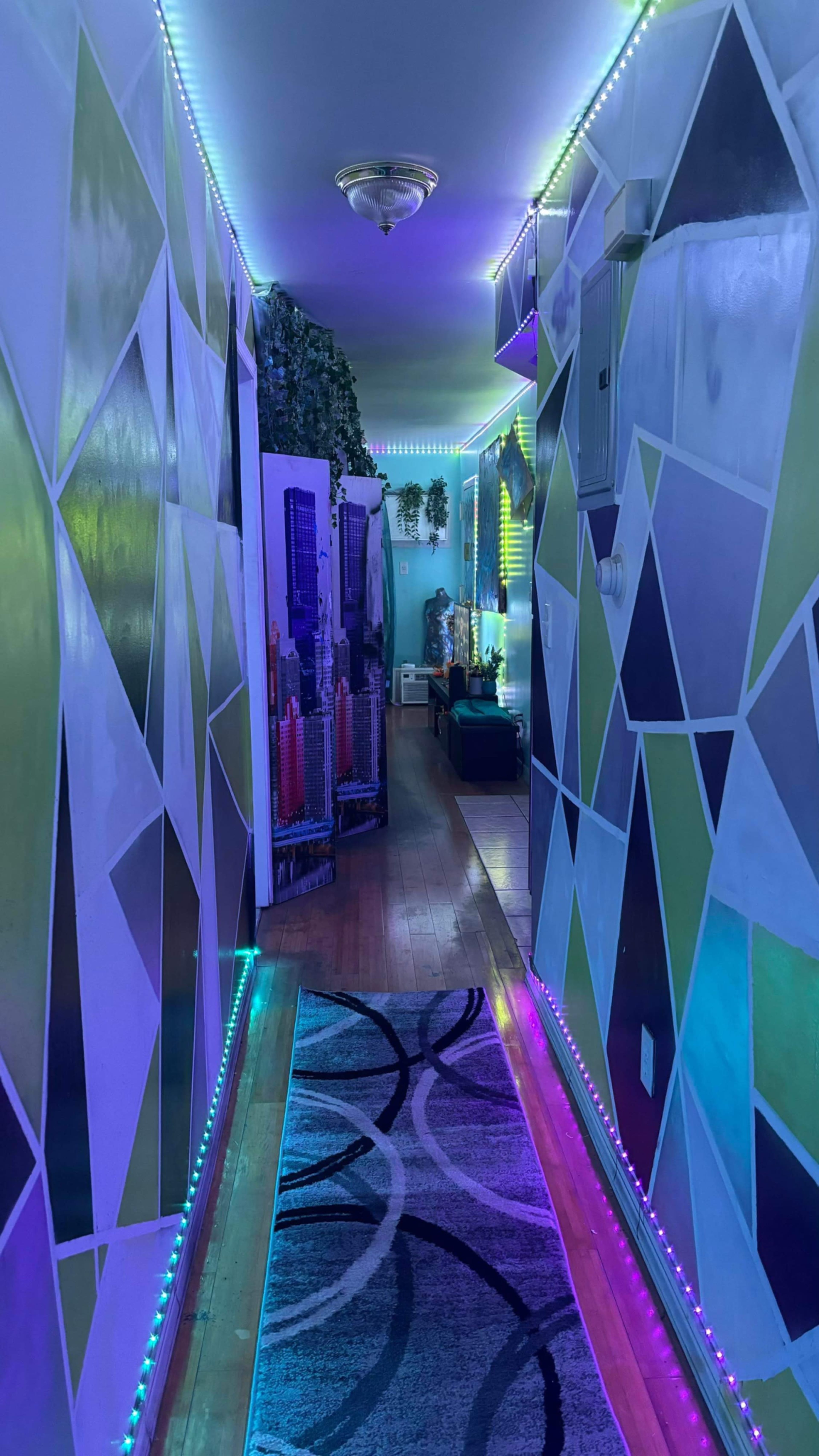 A narrow hallway features geometrically patterned walls and colorful LED lighting along the ceiling.