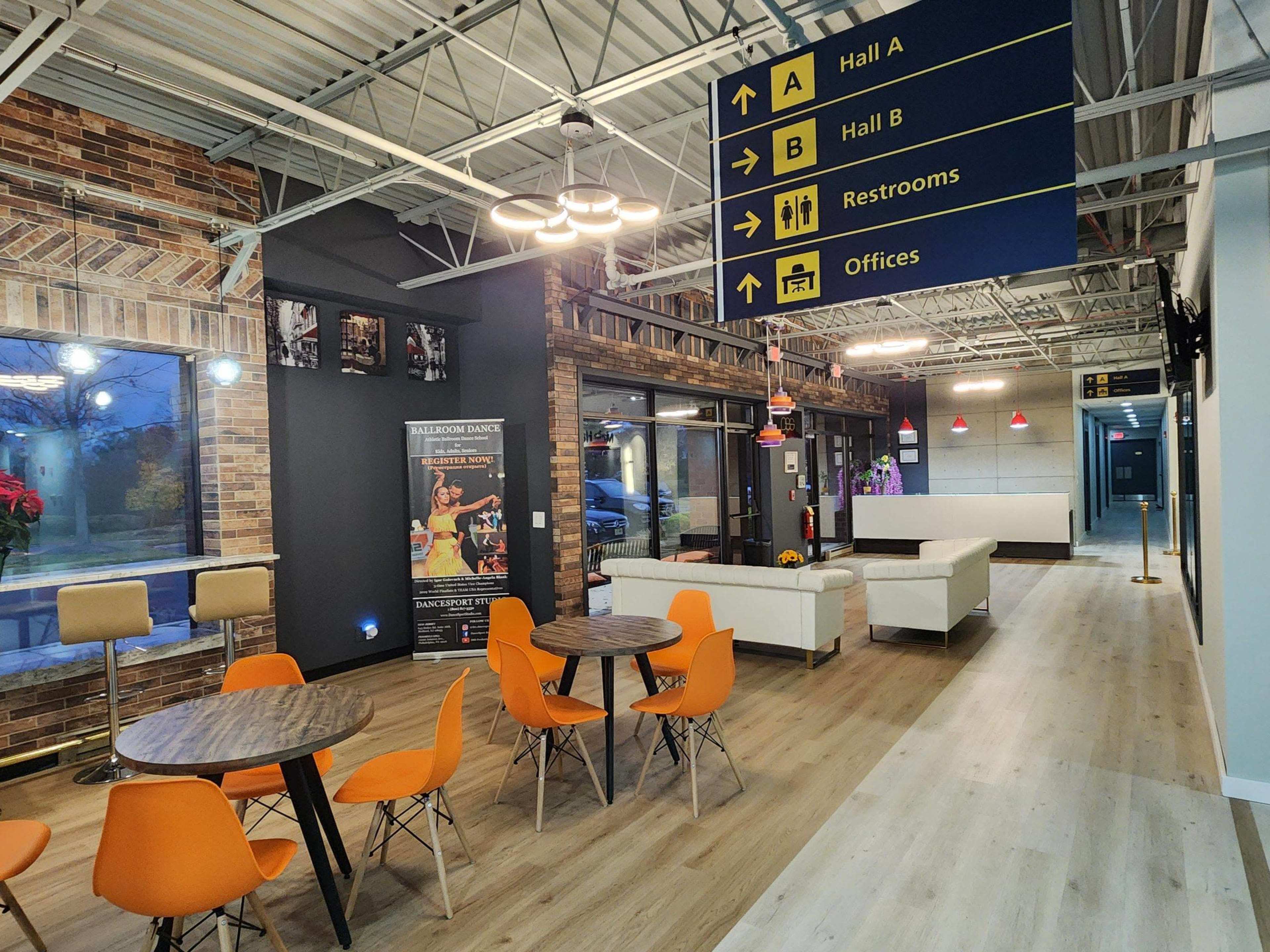 The image shows a modern interior space with seating areas, a reception desk, and directional signs indicating the locations of various facilities.