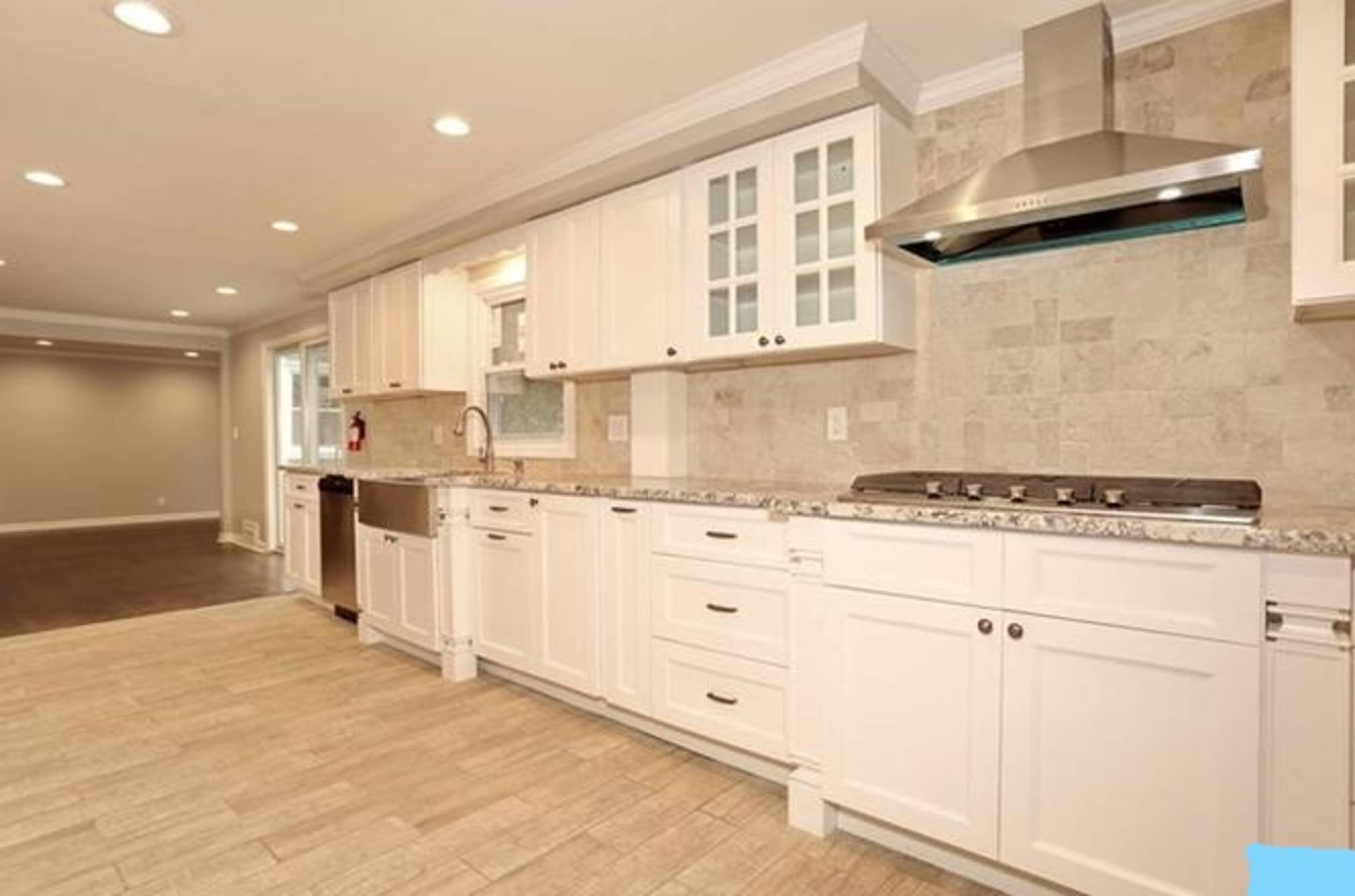 A modern kitchen with white cabinets, a stainless steel range hood, and a tiled backsplash, featuring a countertop with a double sink and a combination of built-in and under-counter appliances.