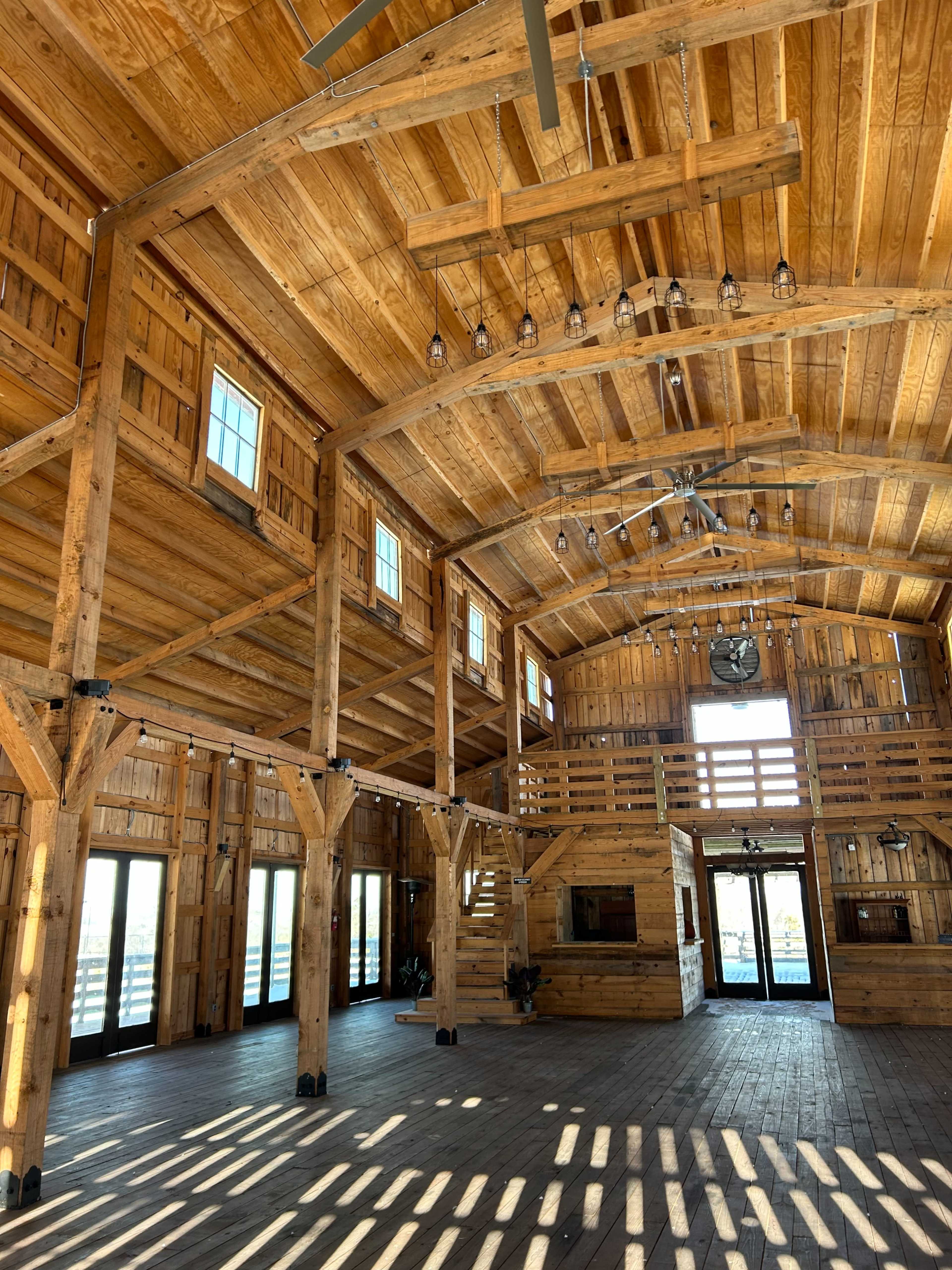 The interior of a spacious barn with wooden beams, large windows, and a high ceiling.