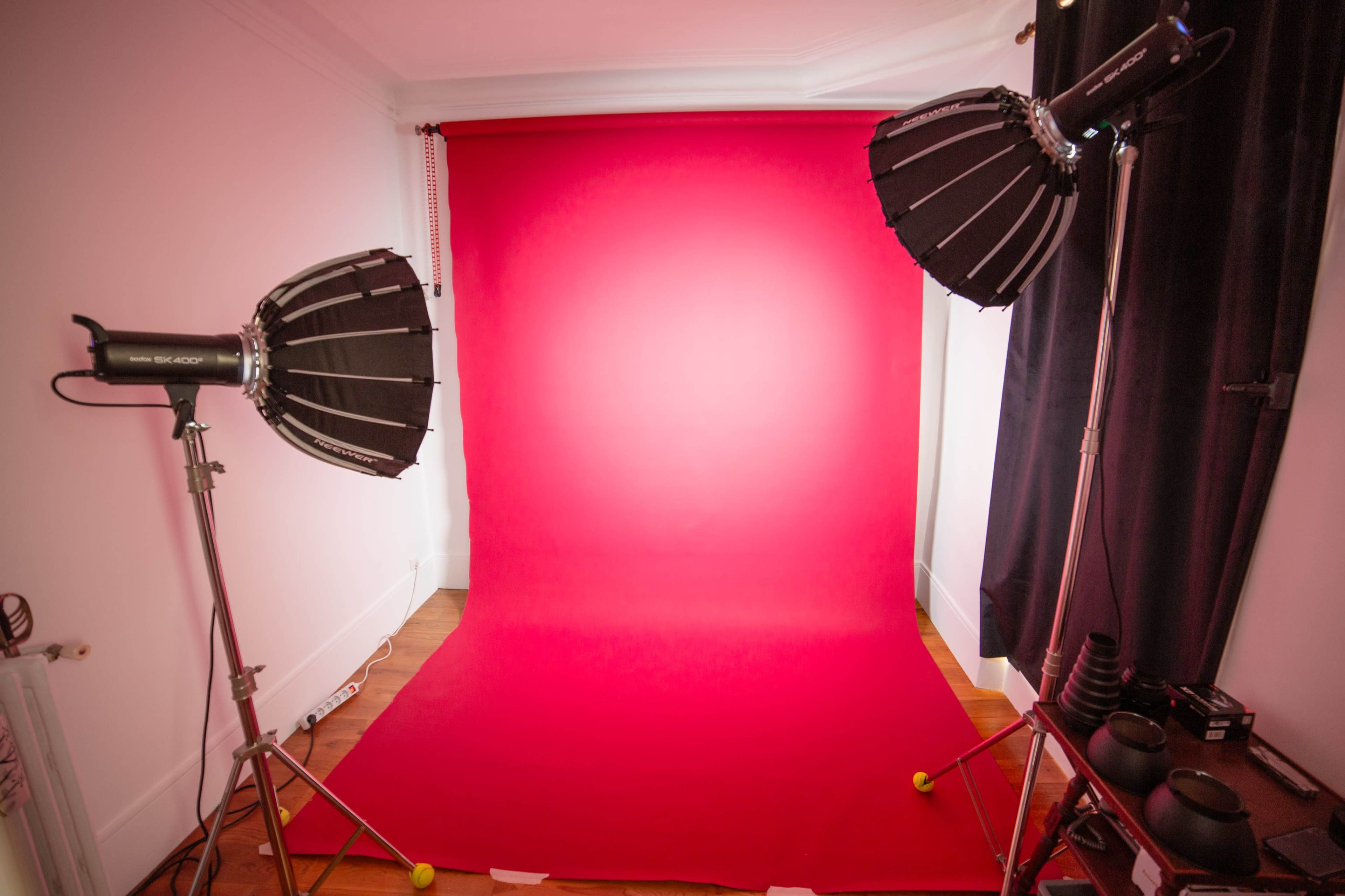 The image shows a photography studio setup with a red backdrop and two lighting fixtures positioned on either side.