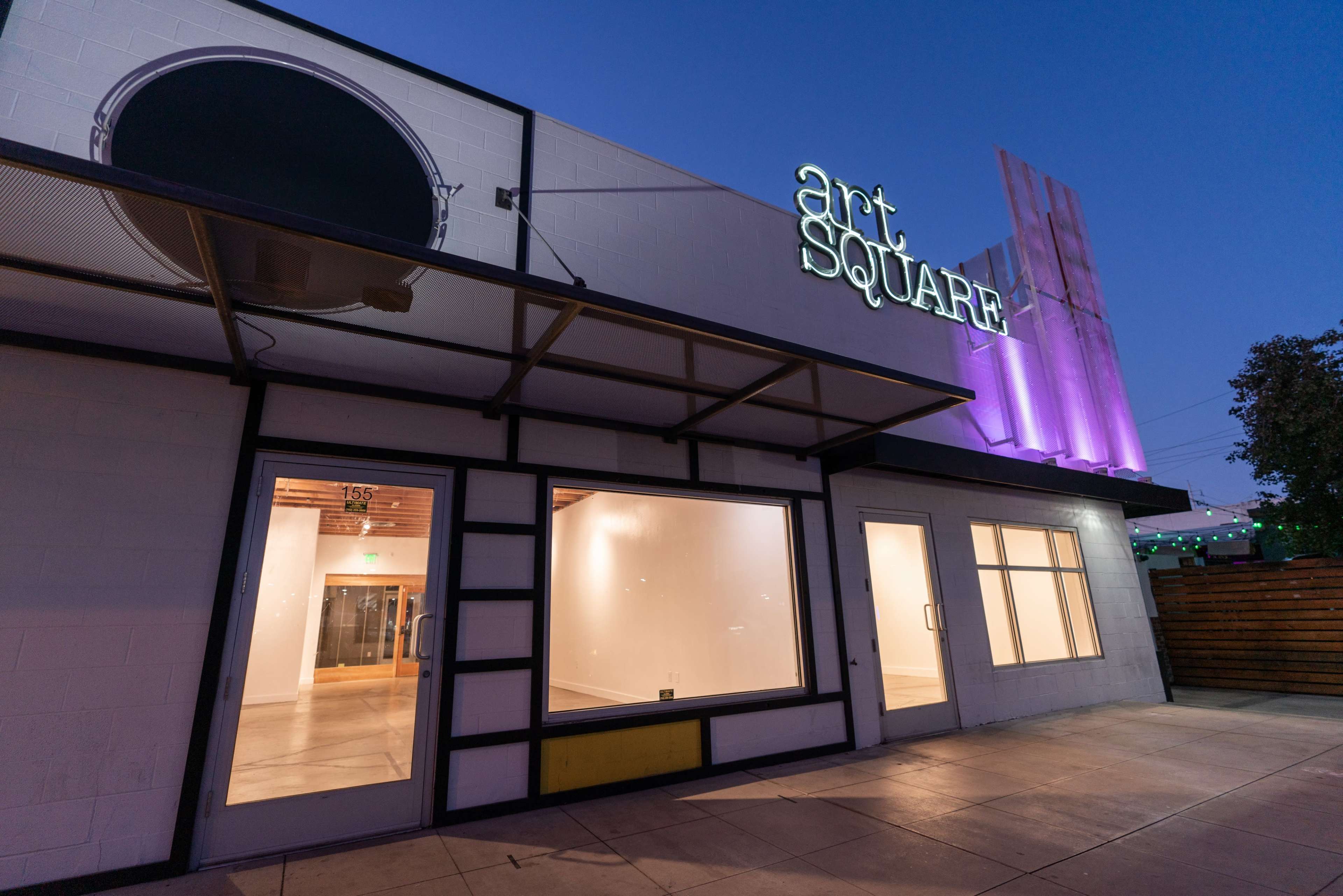 The exterior of a building with a sign reading "art SQUARE" illuminated against a twilight sky, featuring large windows and a minimalist design.