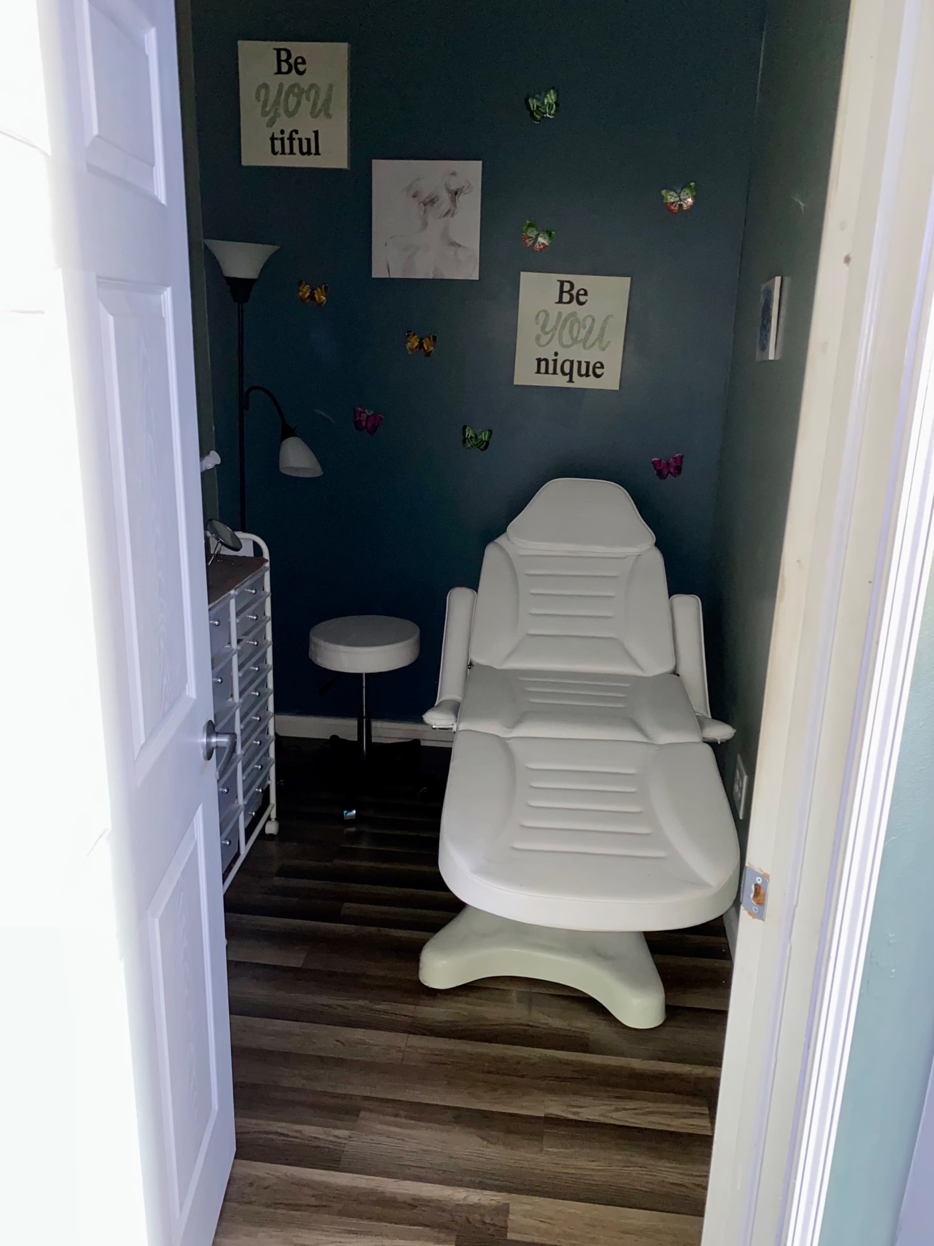 A small treatment room features a white reclining chair, a lamp, and a side table, with butterfly decorations and motivational wall art.