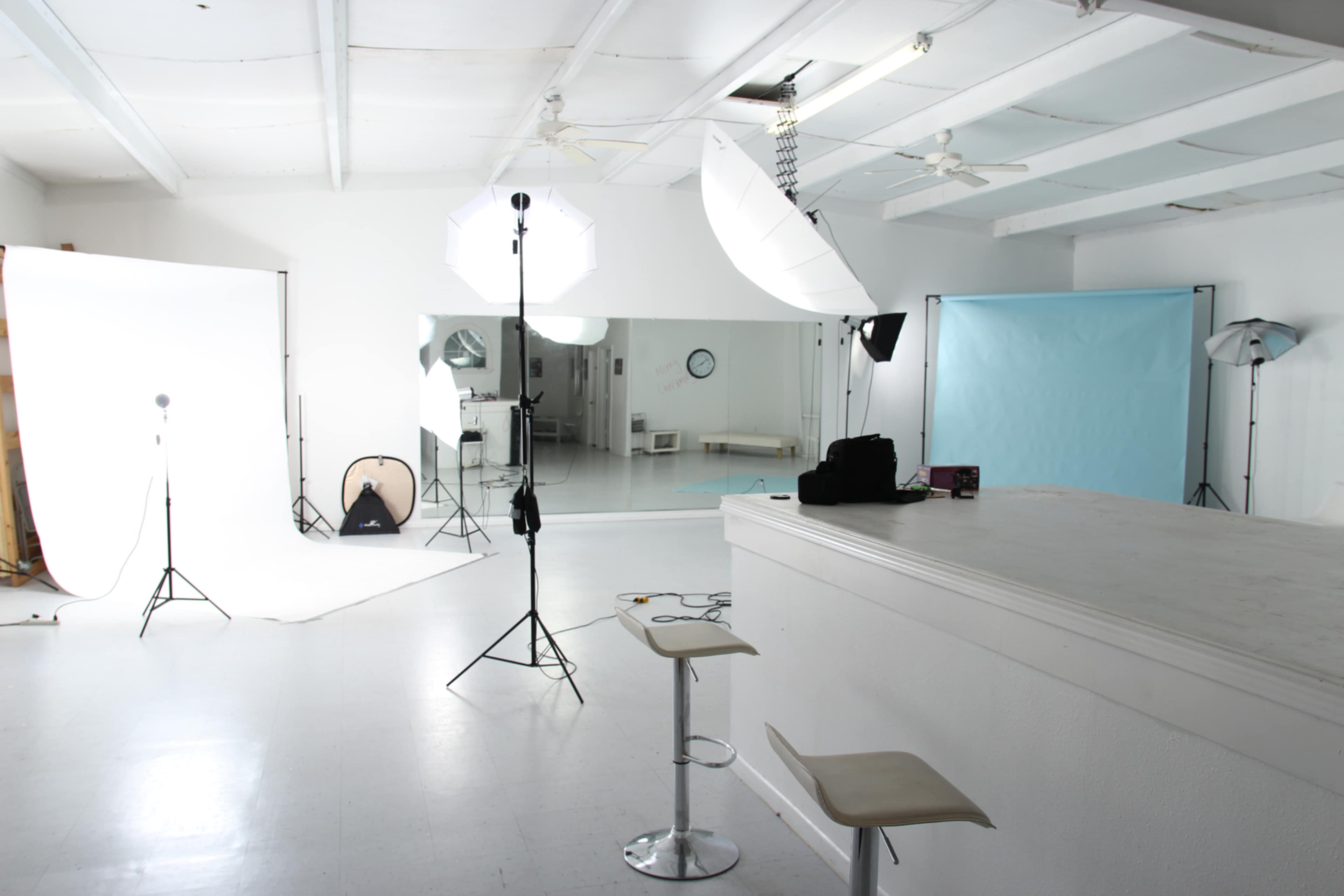 A photography studio features lighting equipment, backdrop stands, and a bar area with stools.