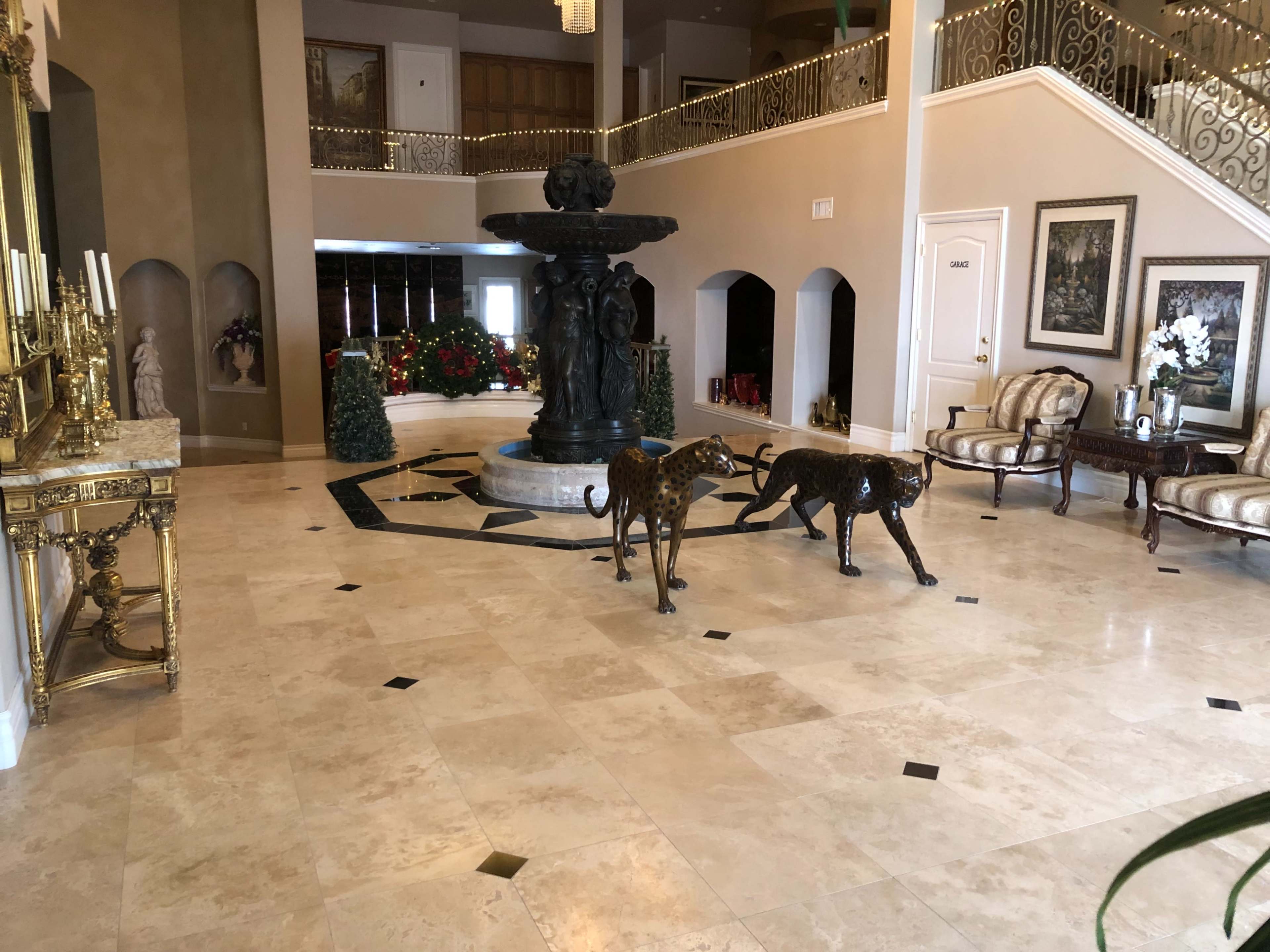 A spacious foyer with a marble floor, featuring a central fountain and two bronze leopard sculptures on display.