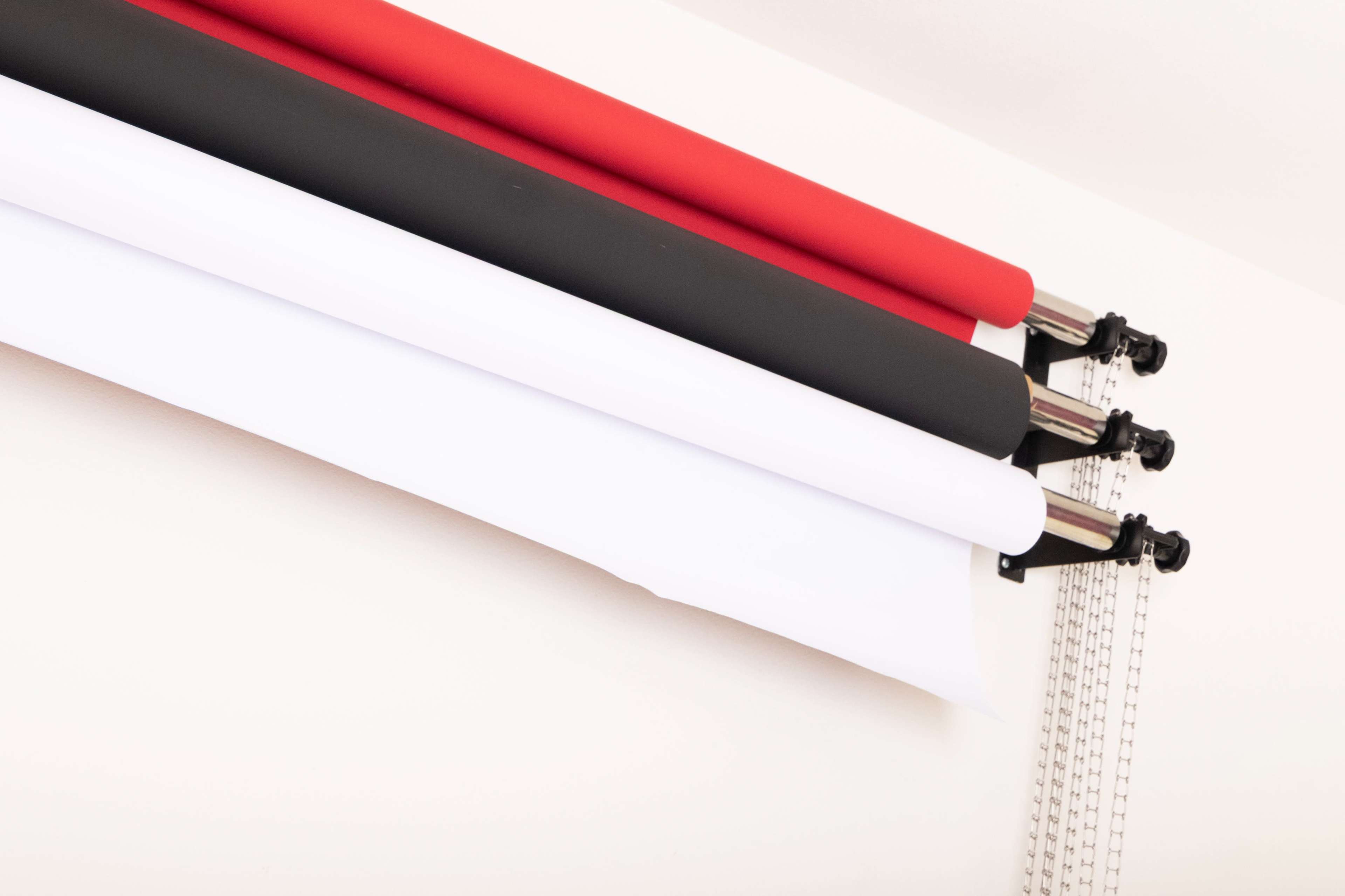 The image shows three rolls of backdrop paper in black, white, and red mounted on a wall.