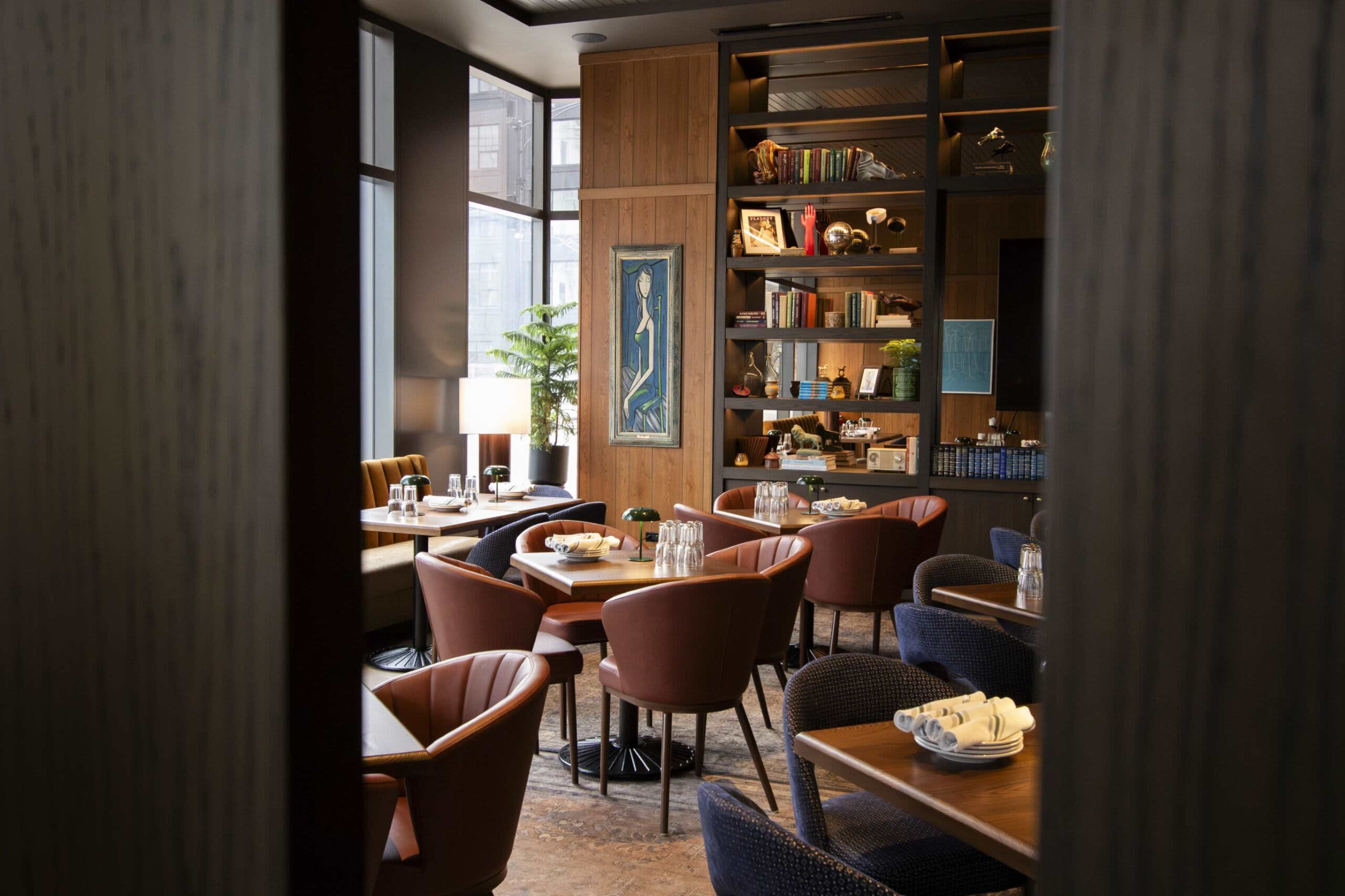 The image shows a well-furnished restaurant with wooden paneling, tables set for dining, and shelves displaying books and decor.