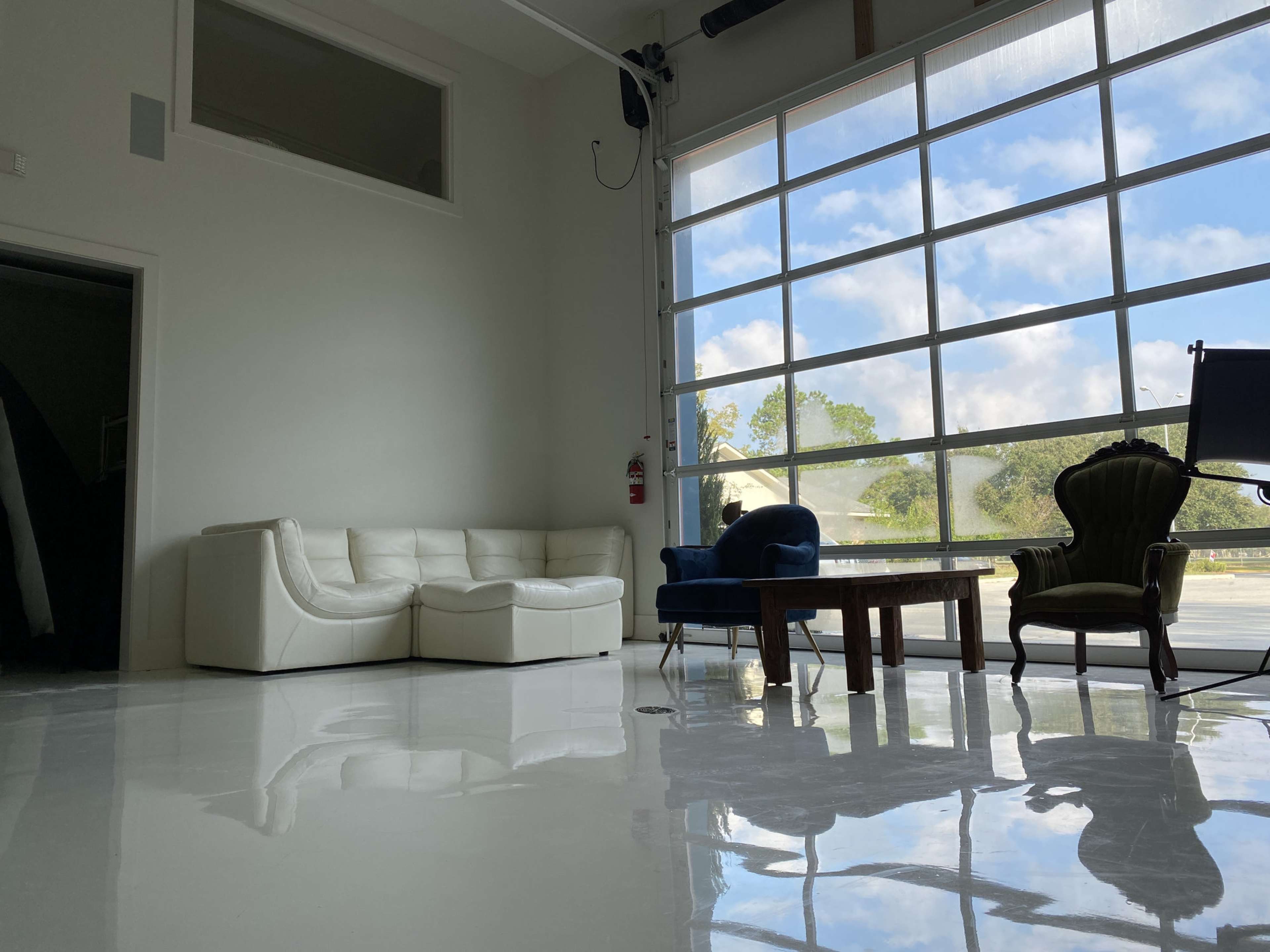 A modern interior with a white sectional sofa, two distinct chairs, and a wooden table, all situated on a glossy floor beside large glass windows.
