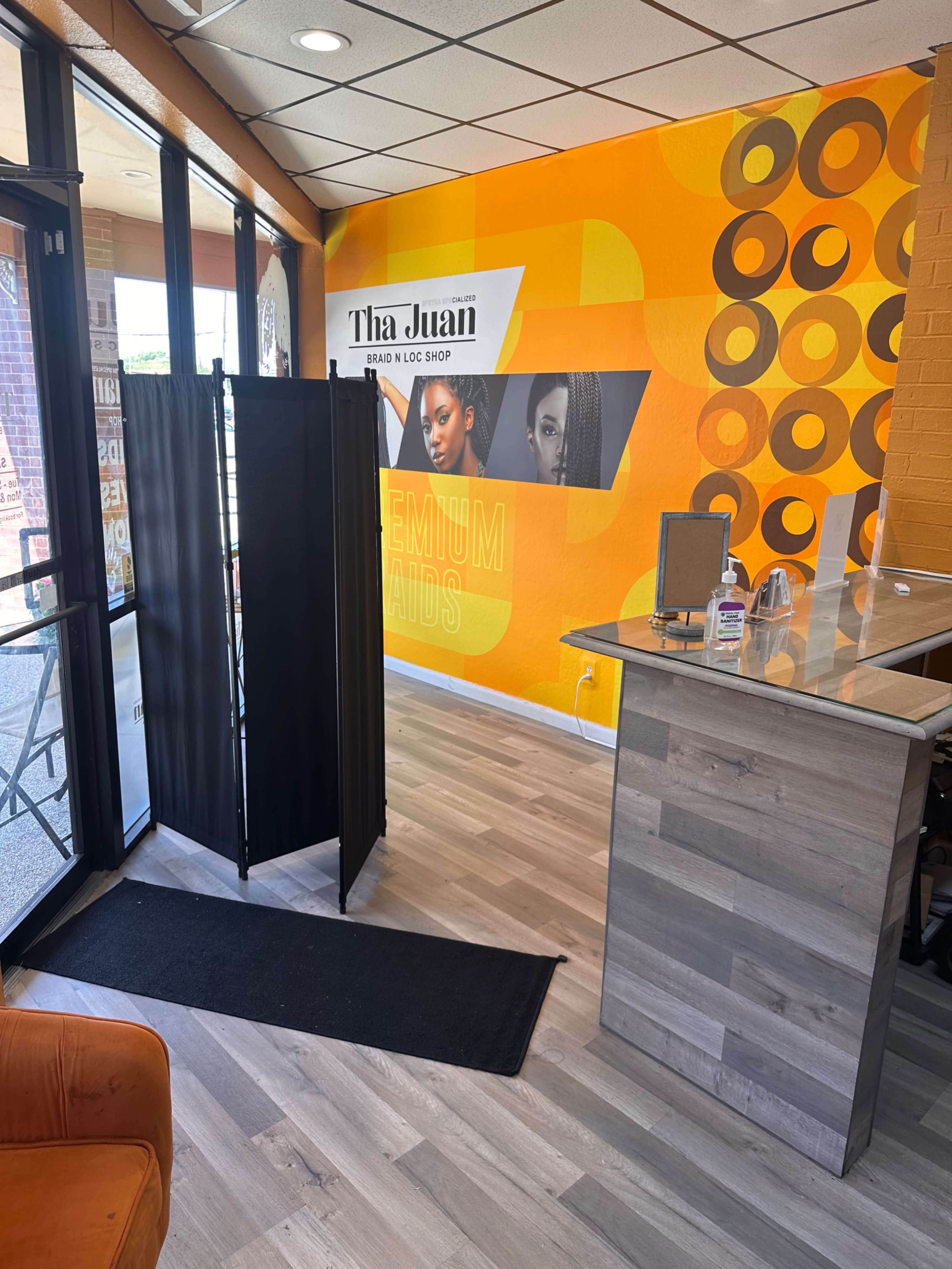 The interior of a salon features a reception area with a black privacy screen and an orange accent wall displaying promotional graphics.
