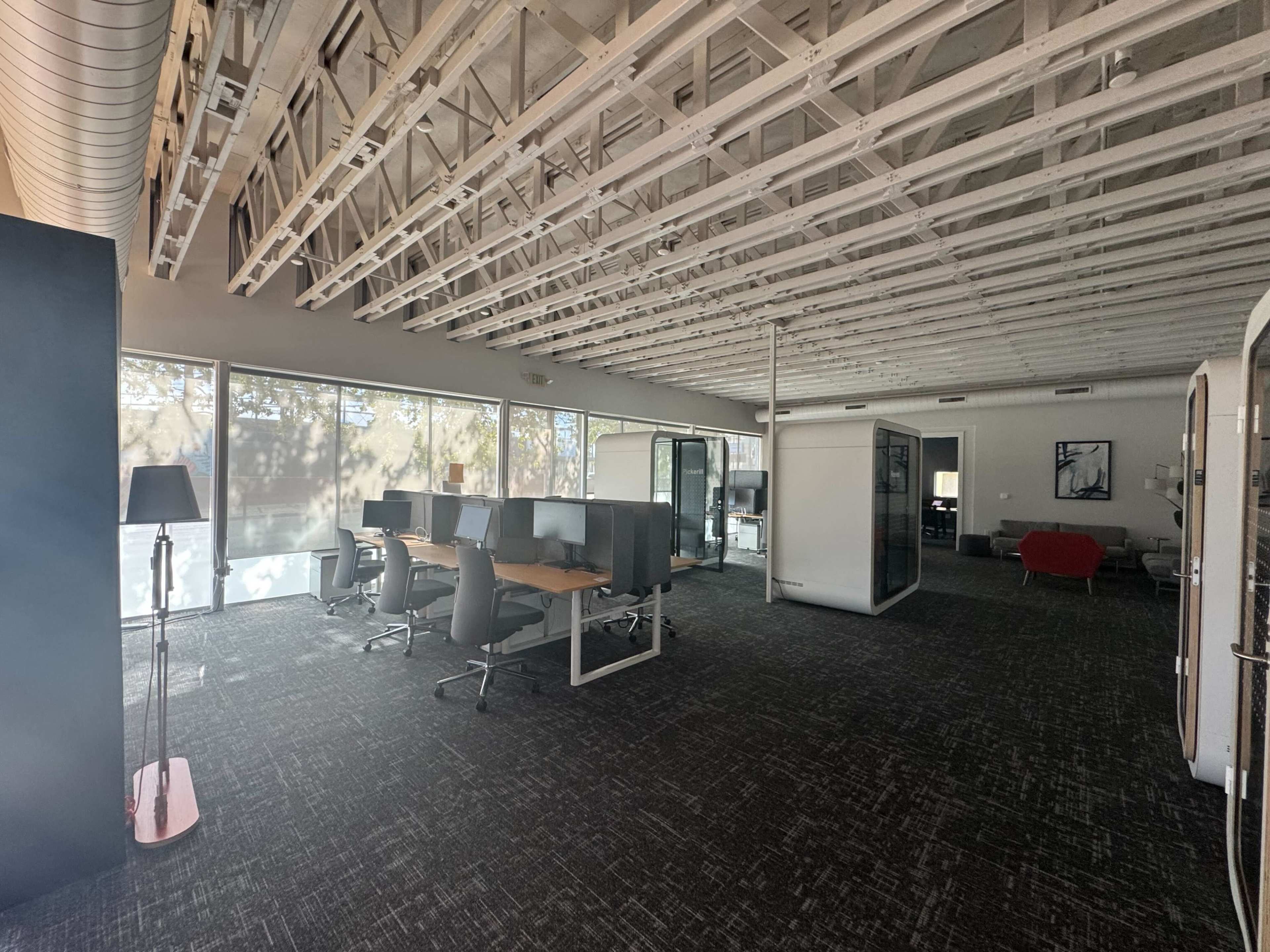 The image shows a spacious, modern office with workstations, glass meeting rooms, and a lounge area.