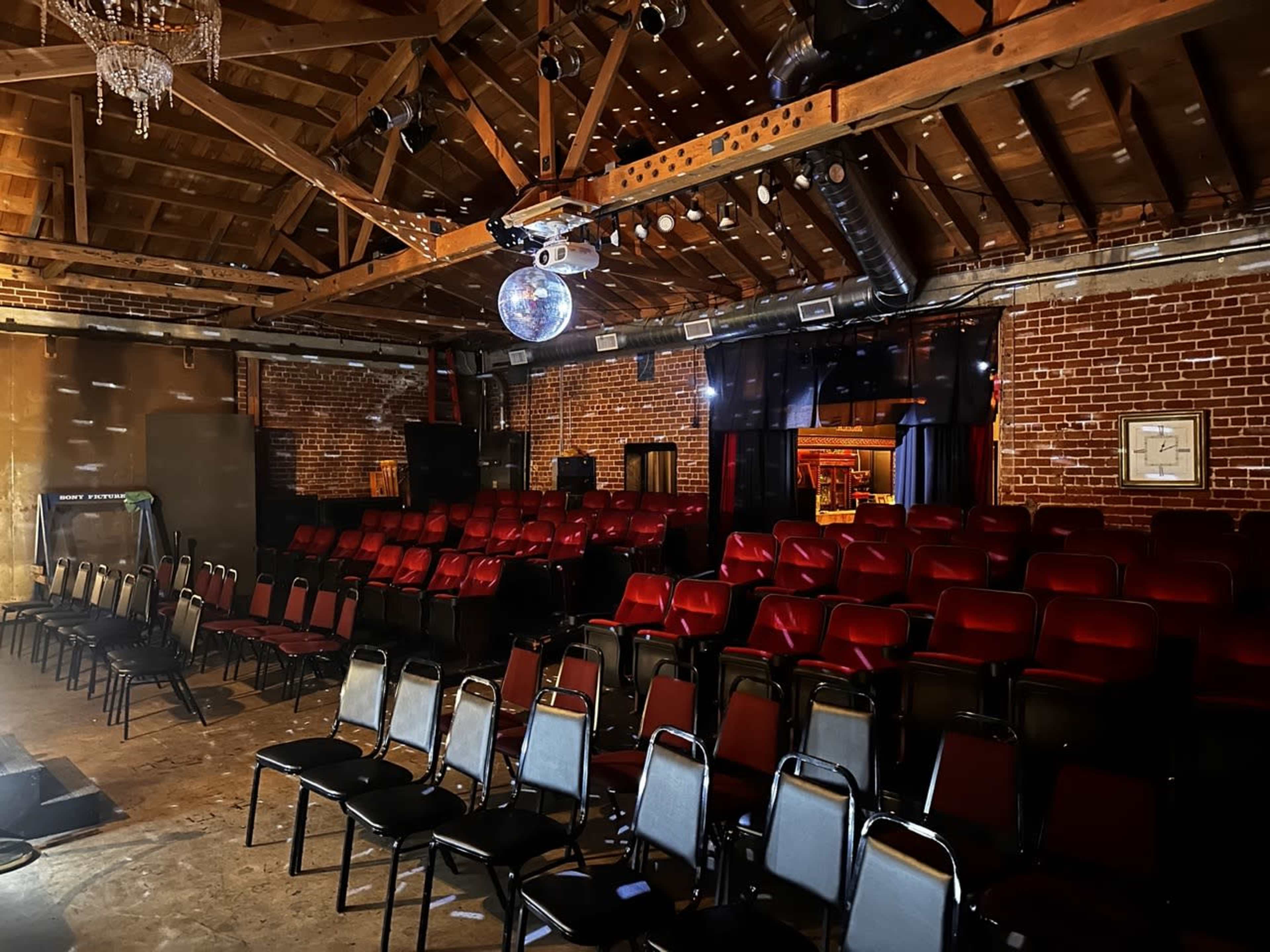 An indoor venue with a seating area arranged with red and silver chairs, a disco ball hanging from the ceiling, and exposed wooden beams overhead.